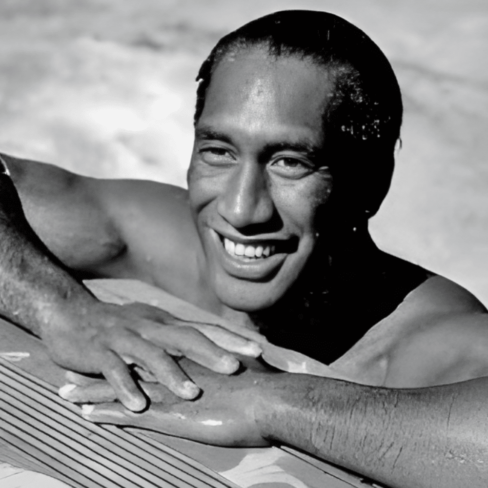 Duke Kahanamoku riding a long wooden surfboard, pioneer of modern surfing.