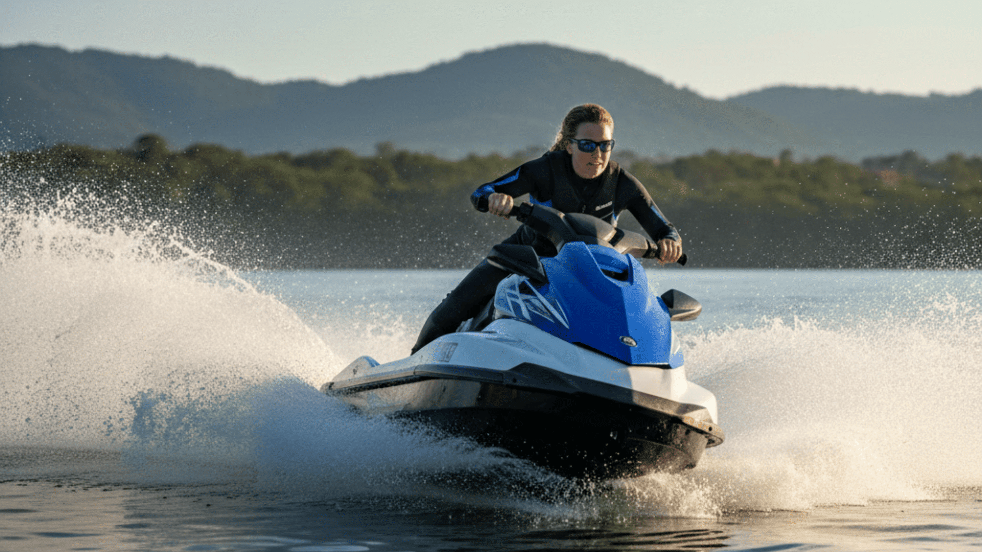 A woman in a black suit rides a blue and white jet ski, showcasing a dynamic water sport scene