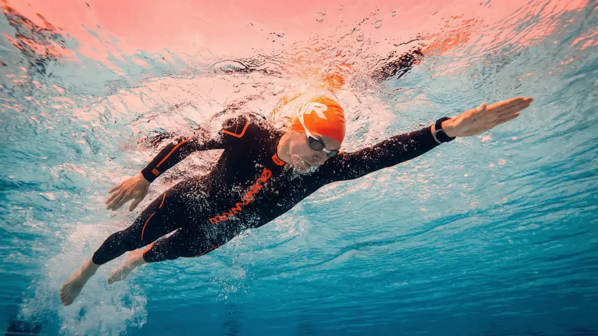 A man in a wetsuit practicing basic open water swimming position.