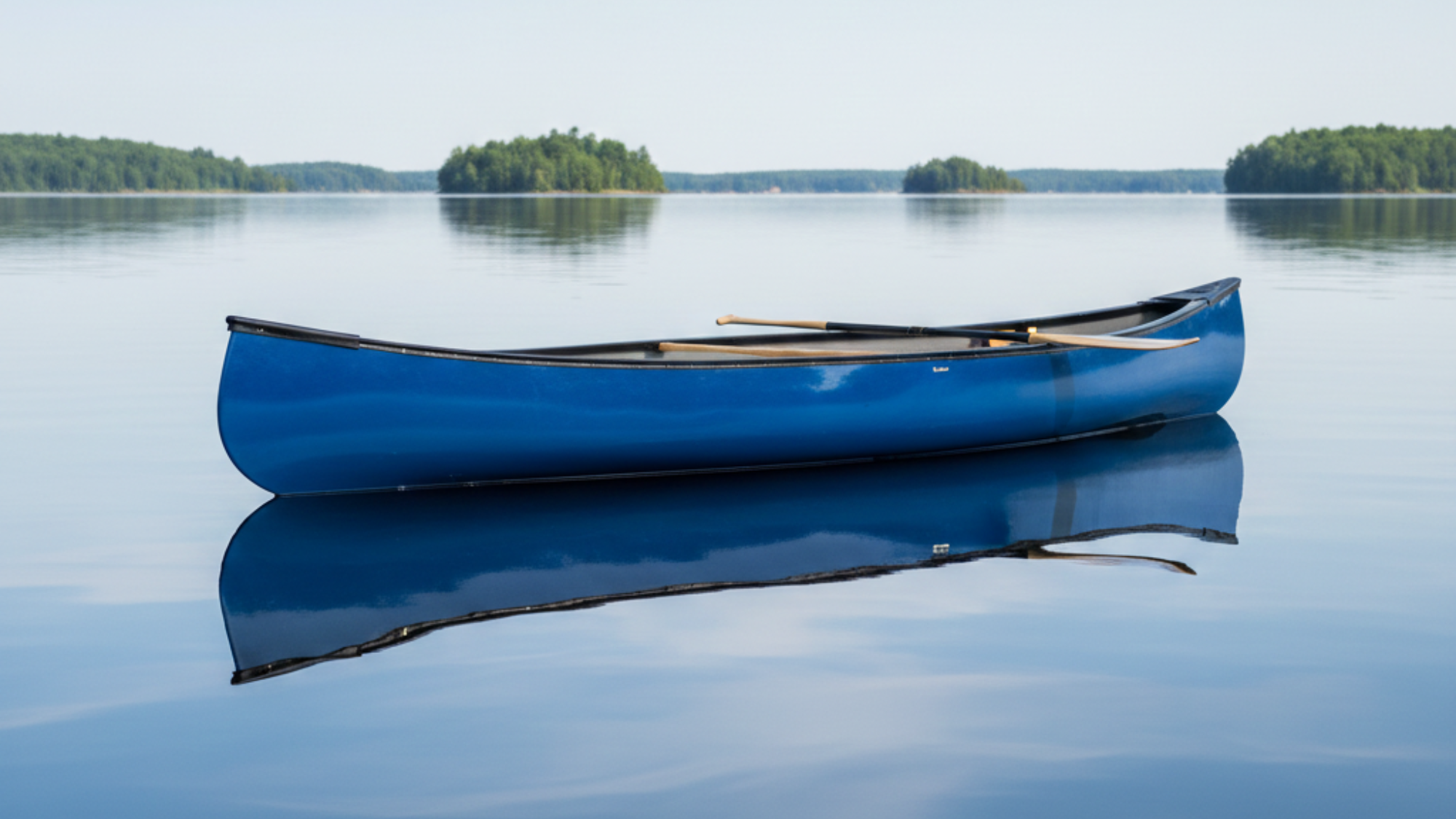 Blue fiberglass canoe floating on calm lake water with paddle inside and small forested islands in the distance.