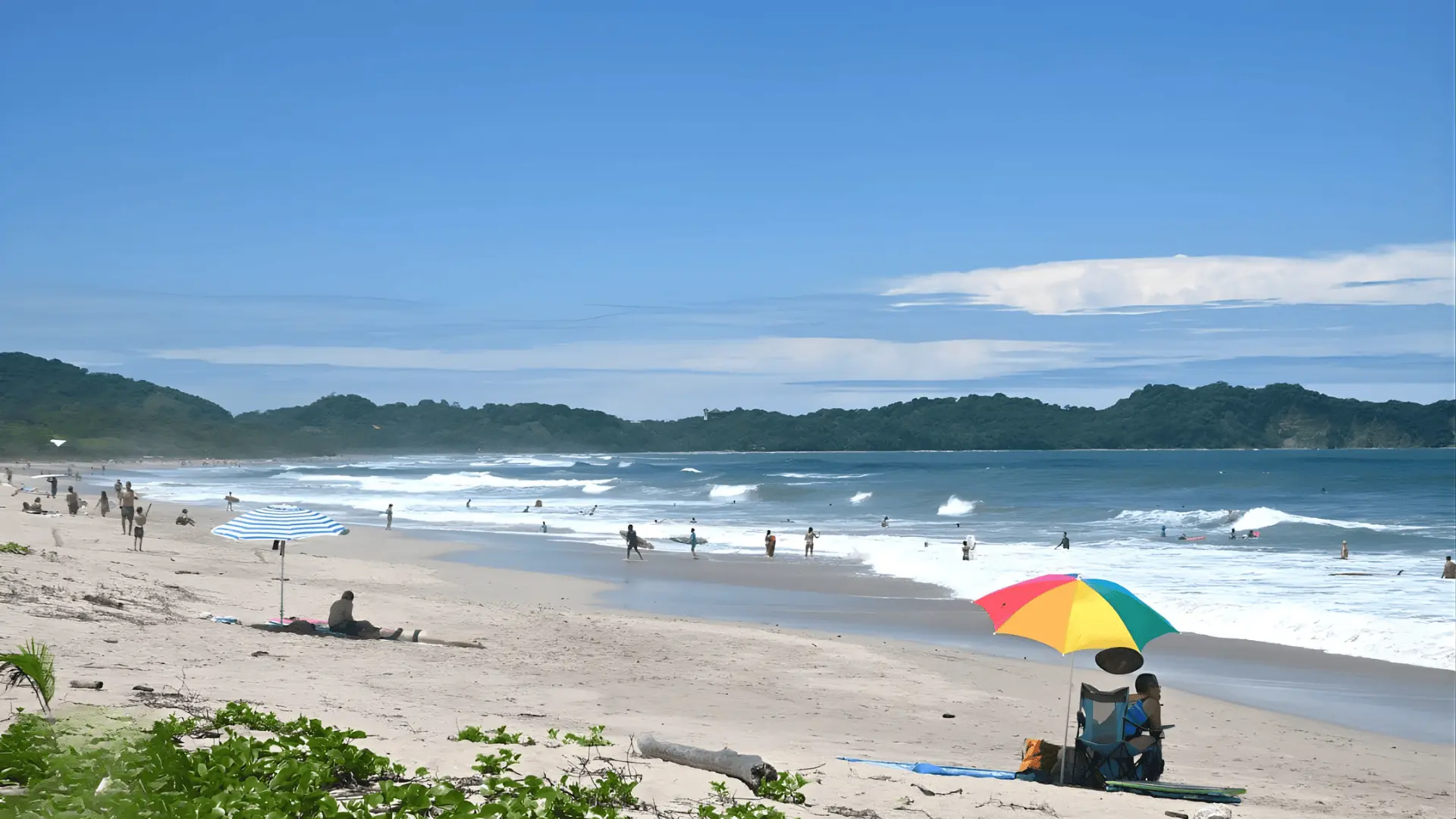 A lively beach at Nosara’s Playa Guiones, showcasing visitors and a bright umbrella amidst the scenic coastal landscape.