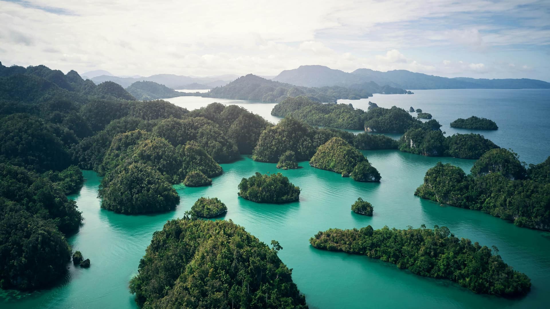 Emerald rainforest islands scattered across a calm turquoise lagoon at sunrise.