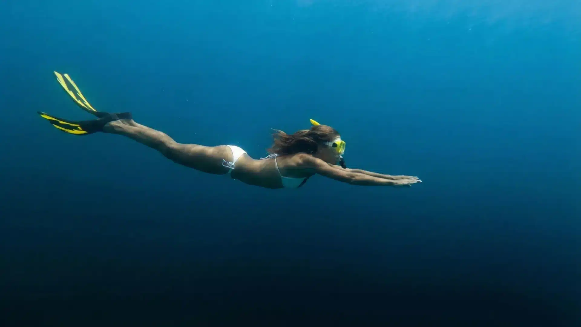 A woman wearing white swim suit skin diving in the ocean.