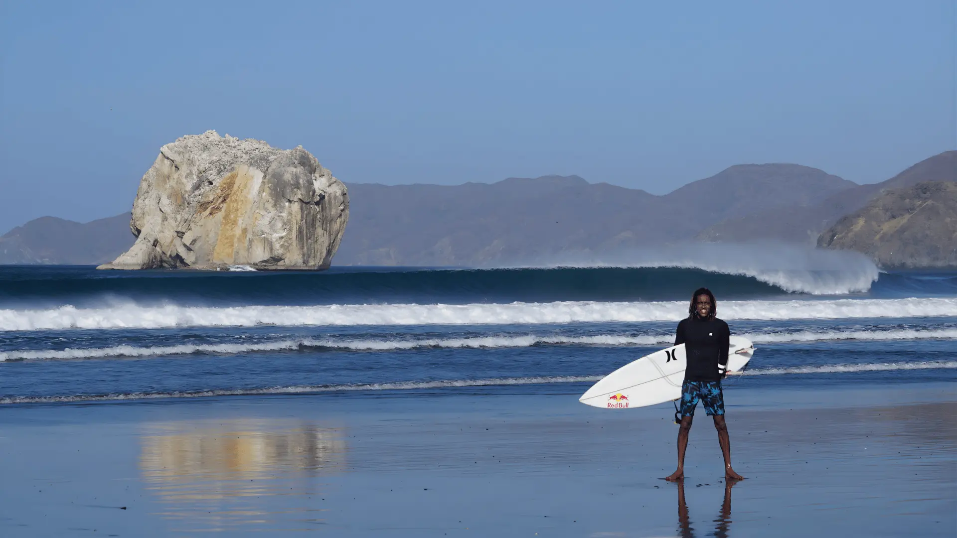 A man on the beach holds a surfboard, ready to surf the powerful waves at Witch’s Rock in Santa Rosa National Park.