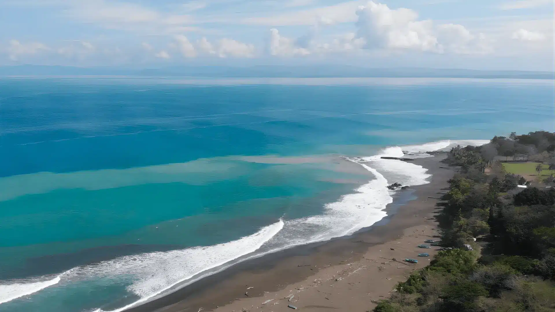Waves crash on the sandy beach of Pavones, with a tranquil body of water reflecting the surrounding rainforest.
