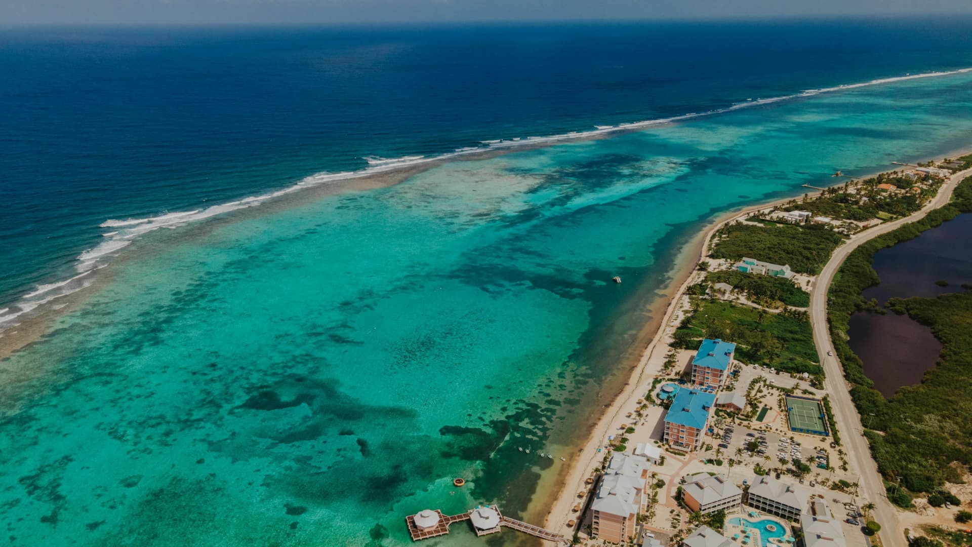 Aerial view of a turquoise reef coastline with resorts, road, and calm blue sea