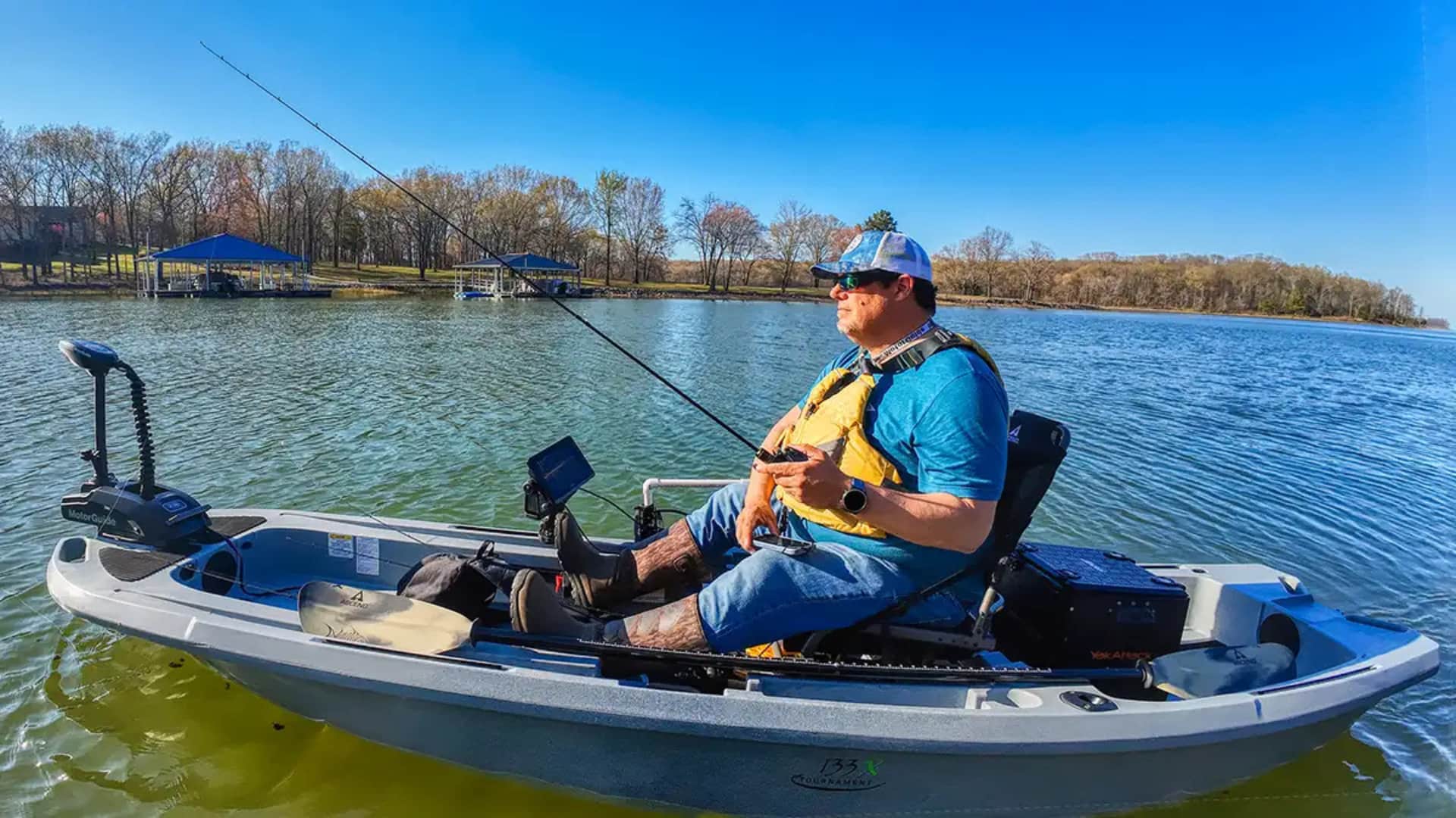Angler in an Ascend fishing kayak on a calm lake under a bright blue sky at rest