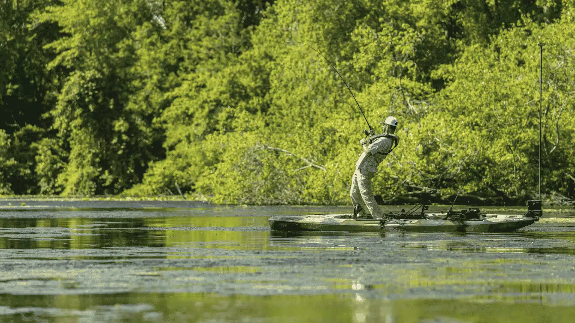 A man fishing from a Hobie Outback kayak on a serene lake, surrounded by calm waters and distant trees