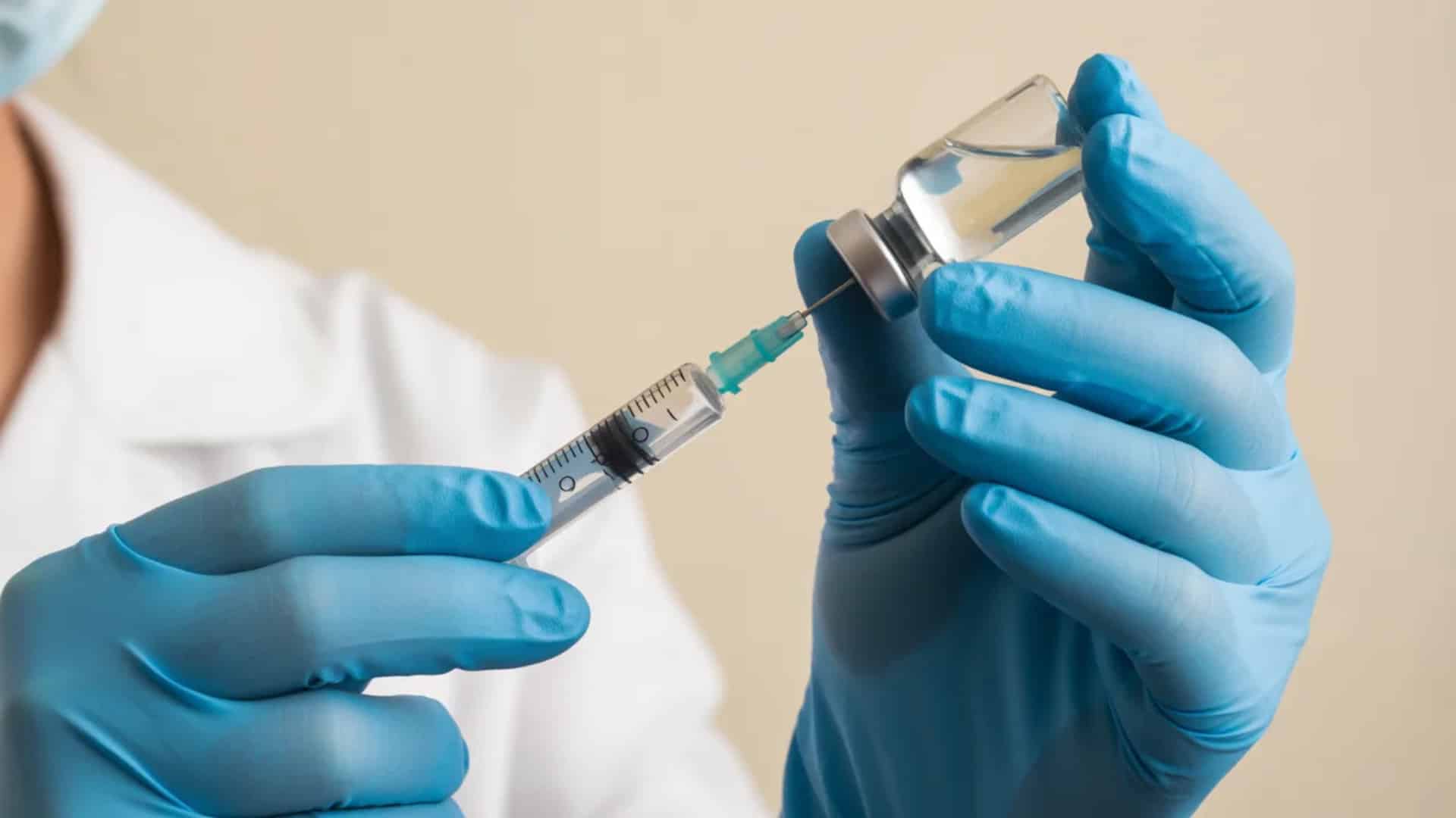 Close-up of gloved medical worker drawing liquid from a vial into a syringe