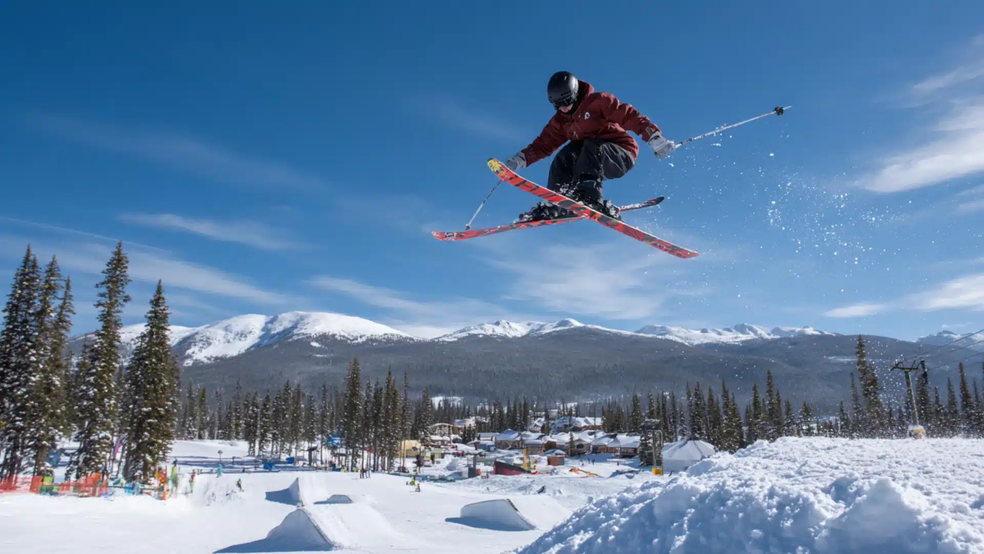 Freestyle skier midair above terrain park jump with snowy peaks in background