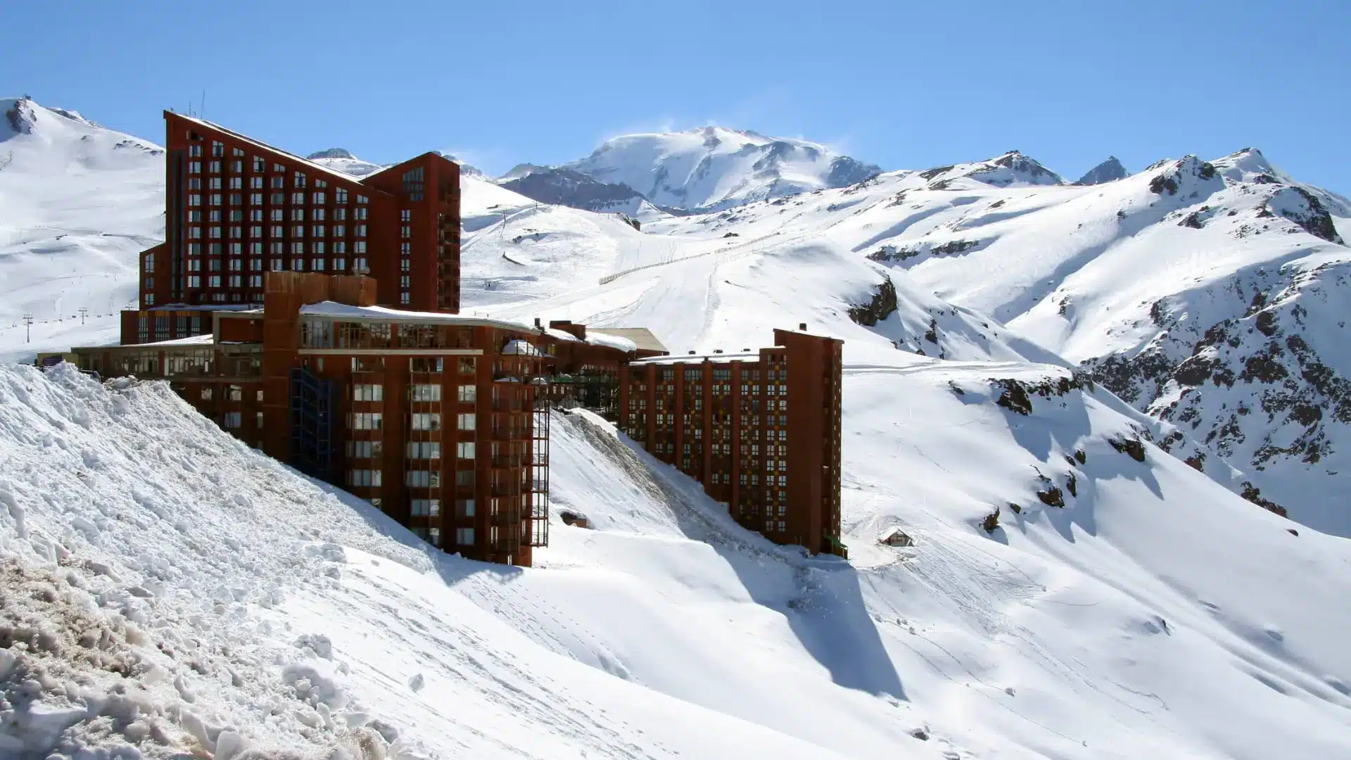 Modern ski resort hotel on a snowy mountain with rugged peaks and clear blue sky