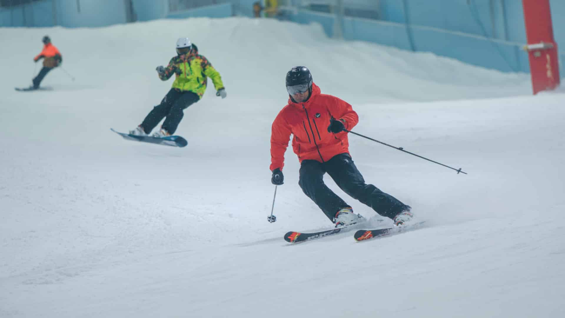 Skier leads snowboarder down indoor slope during a winter practice session drill