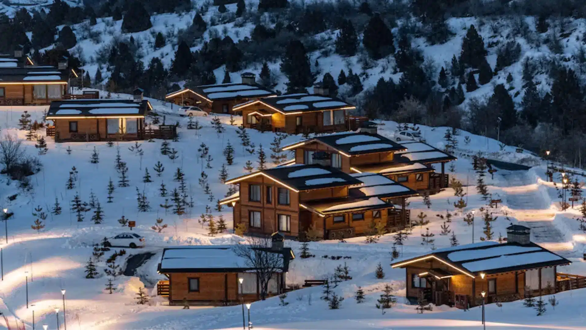 Snow-covered mountain cabins with pine trees, ski area, and rolling hills in a quiet winter landscape