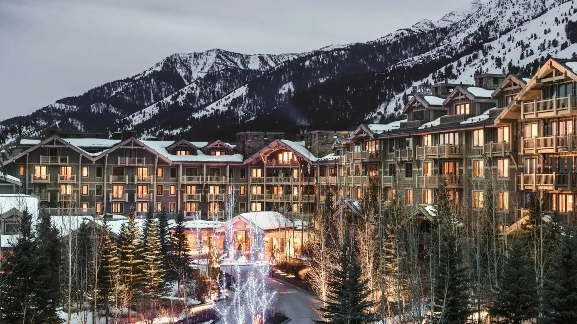 Snow-covered mountain resort with luxury lodges, warm lights, and pine trees set against alpine slopes
