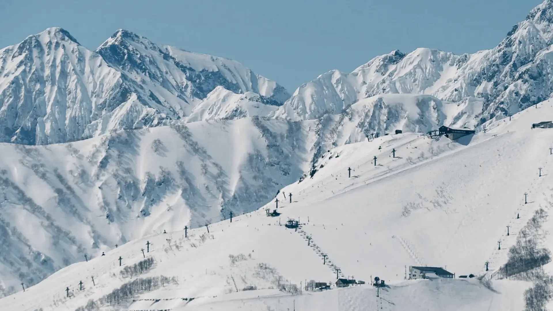 Snow-covered ski mountain with chairlifts, alpine huts, and rugged peaks under a clear winter sky