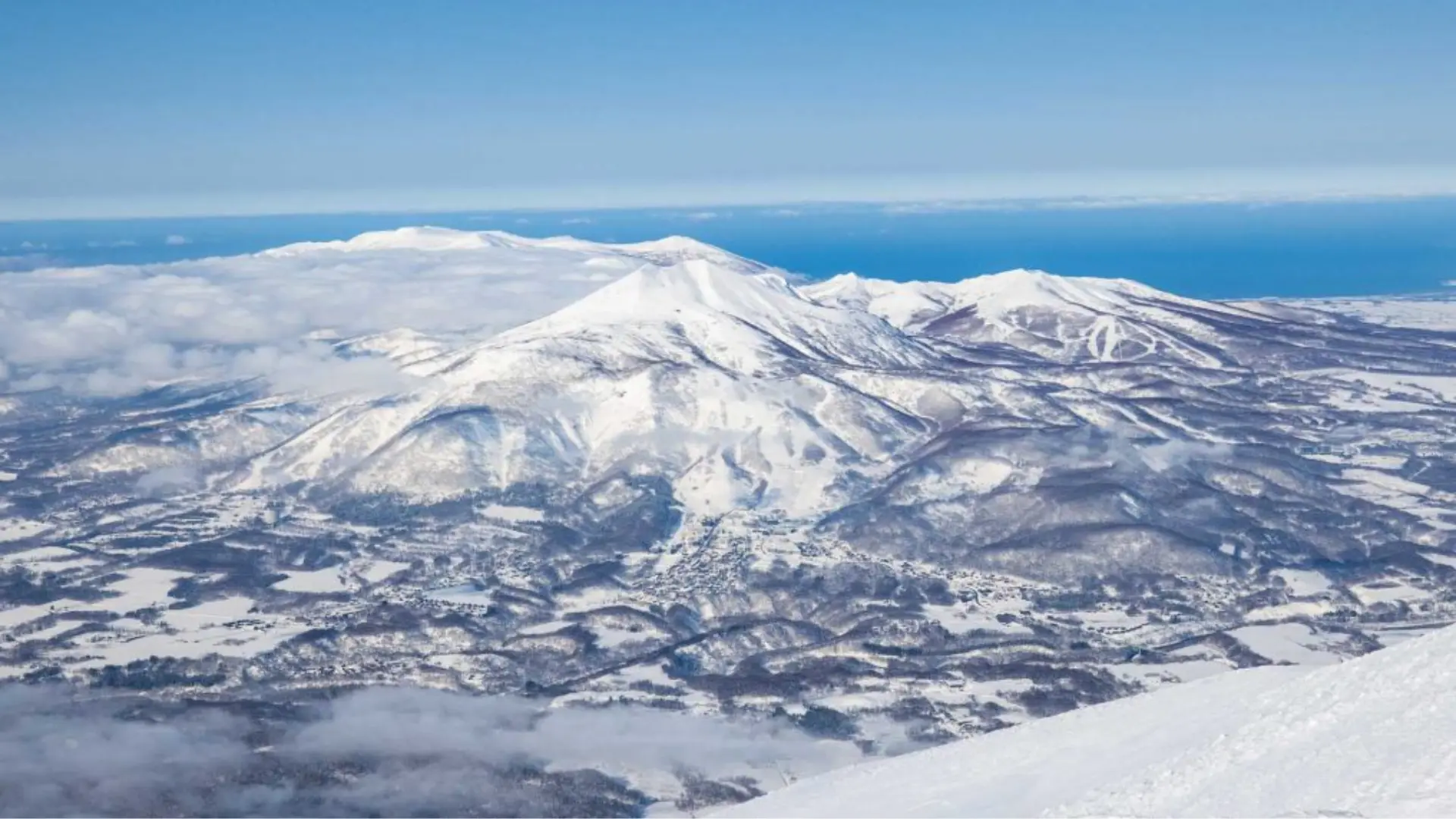 Snow-covered ski resort at dusk with illuminated slopes, mountain village, and winding roads in a winter landscape