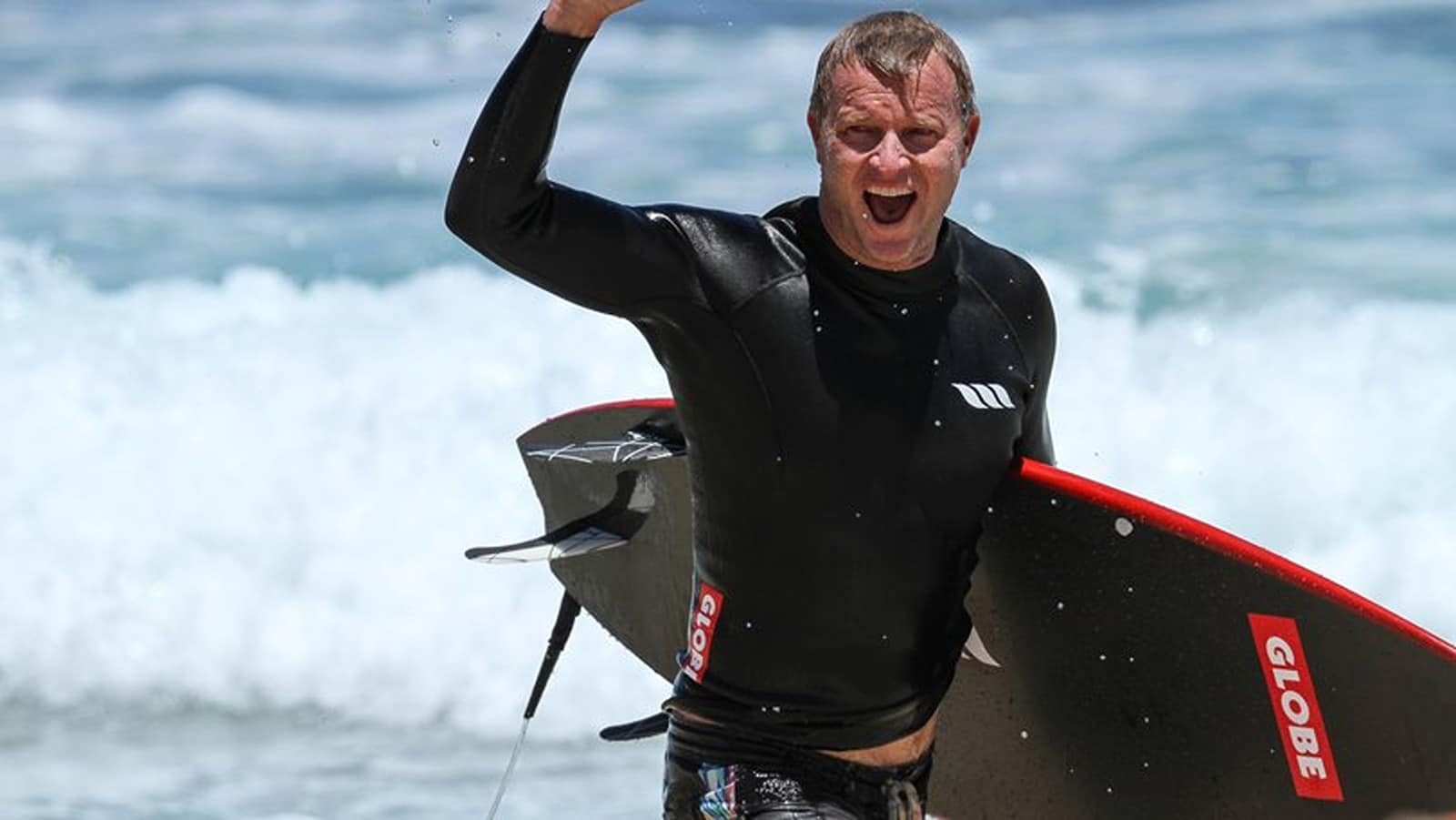 Surfer celebrating on the beach holding a black surfboard after riding waves