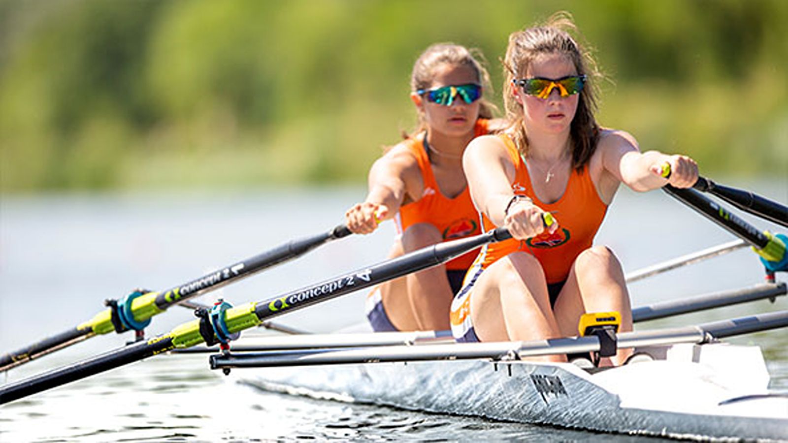 Two female rowers in a crew boat rowing in sync on calm water during training