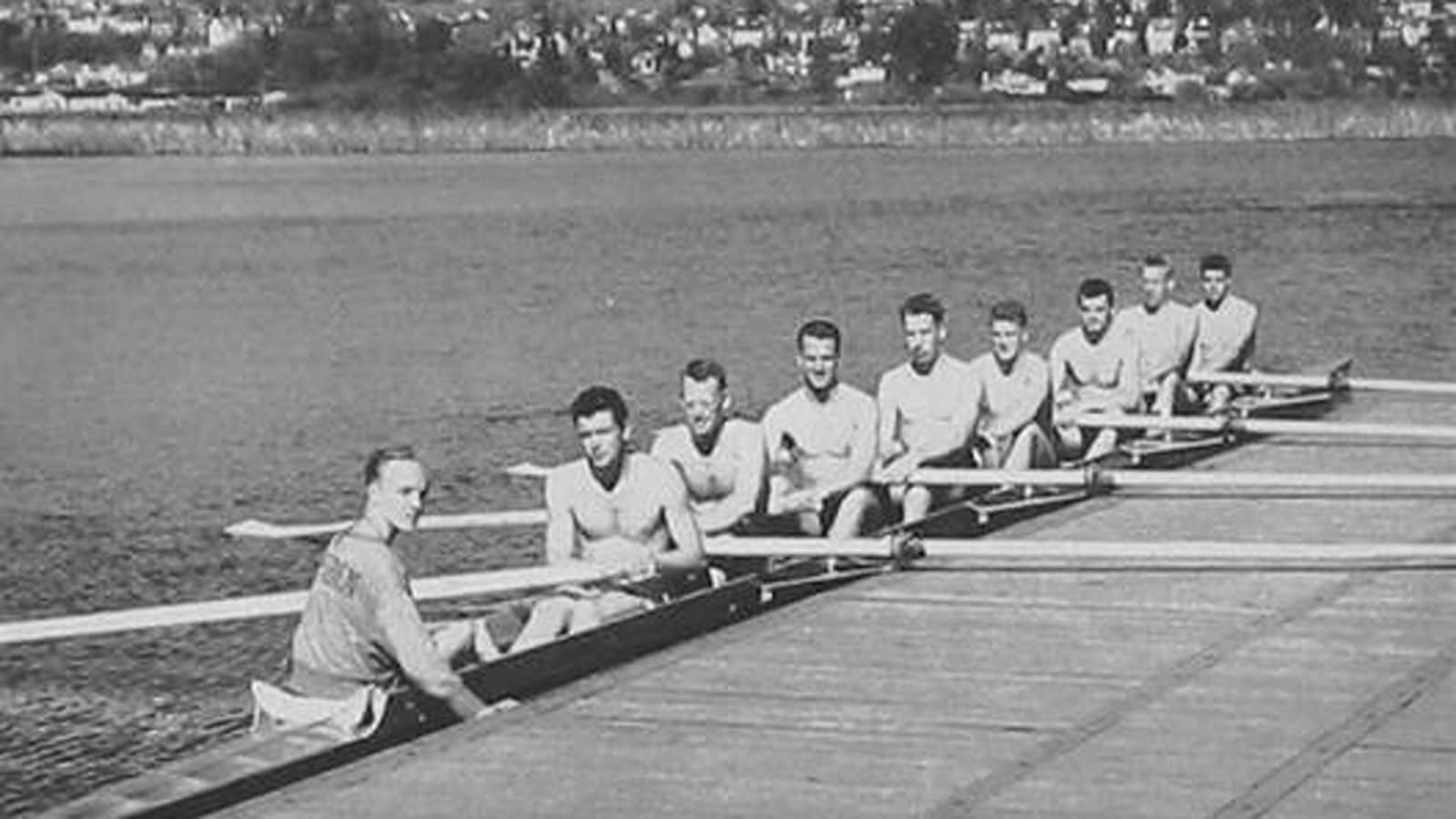 Vintage rowing team sitting in a crew boat near a dock in a black and white photo