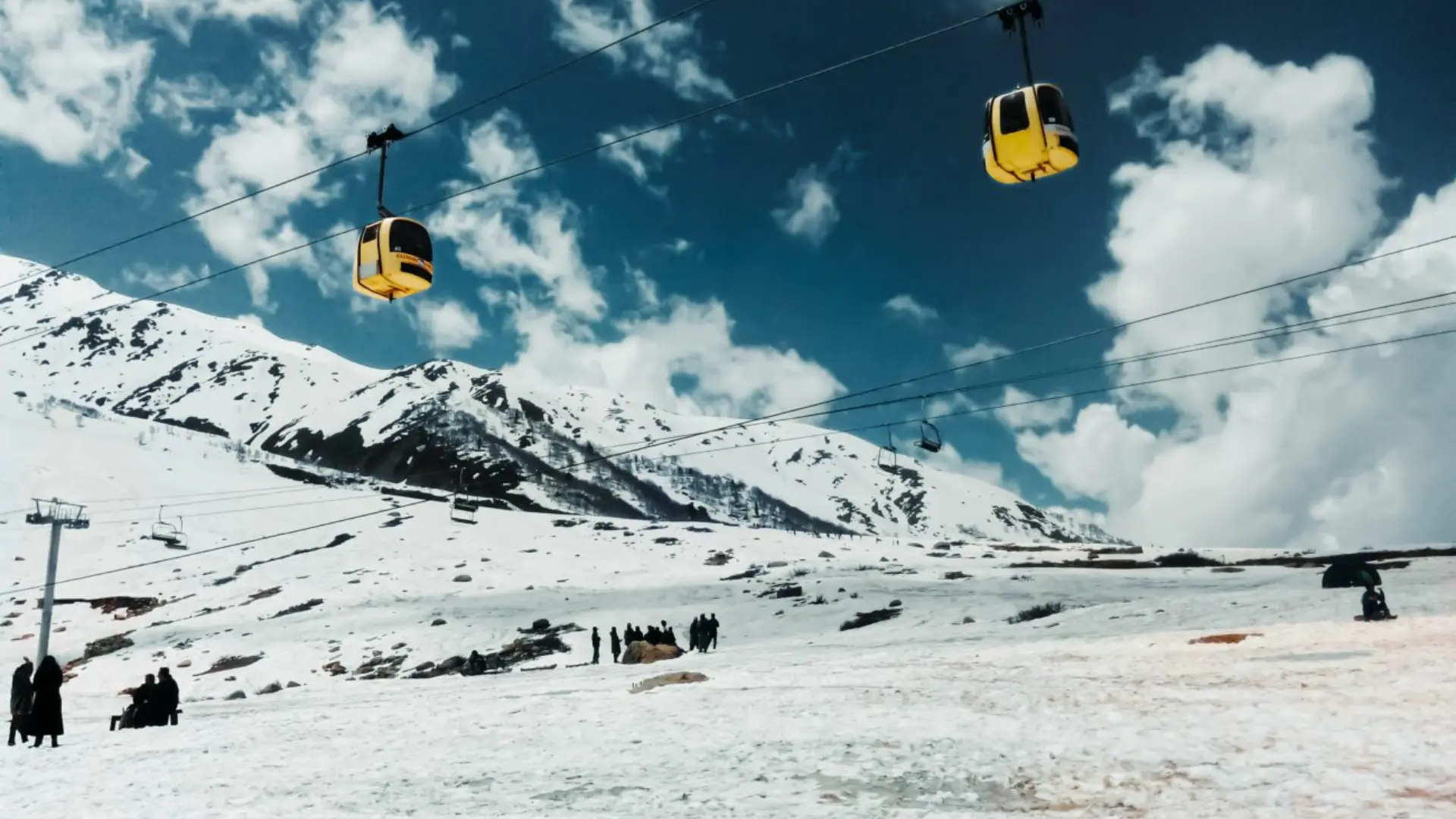 Yellow gondola cable cars over a snowy mountain landscape with skiers and chairlifts under a blue sky