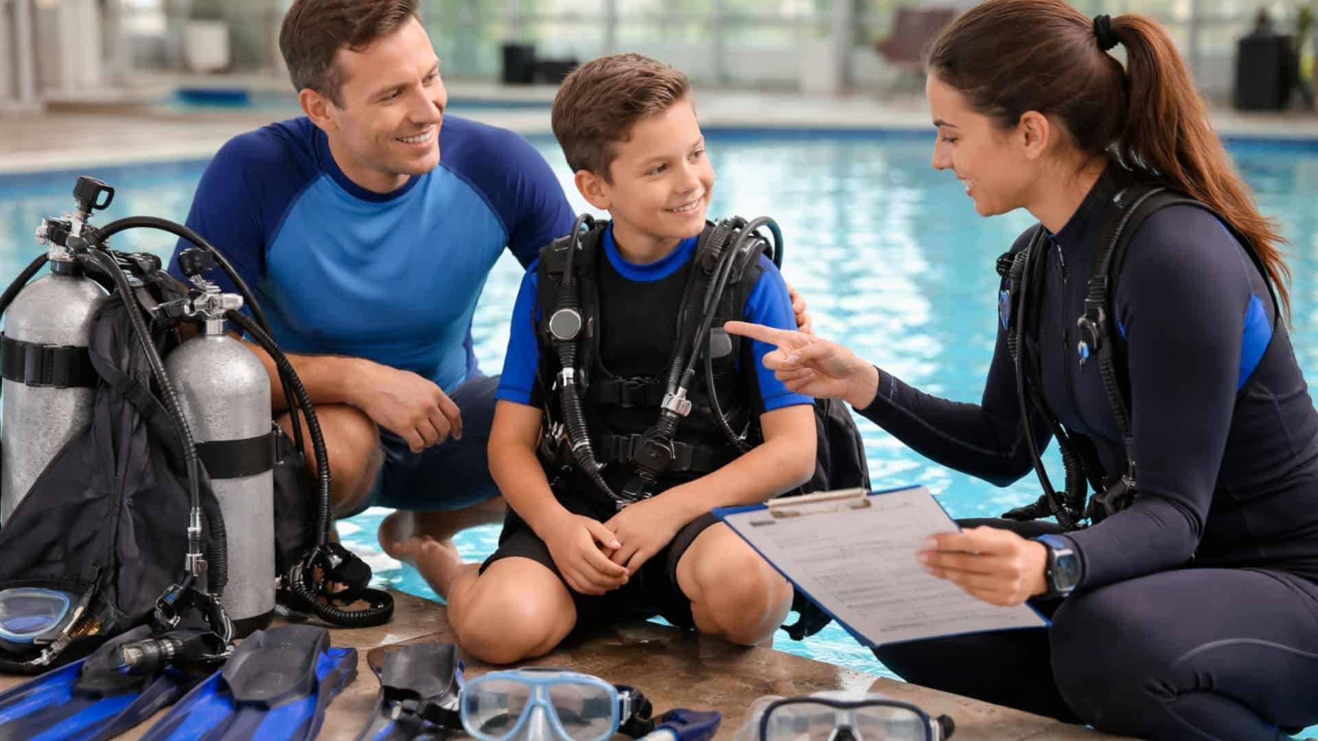 Parent and child reviewing scuba gear beside a pool before beginner dive training