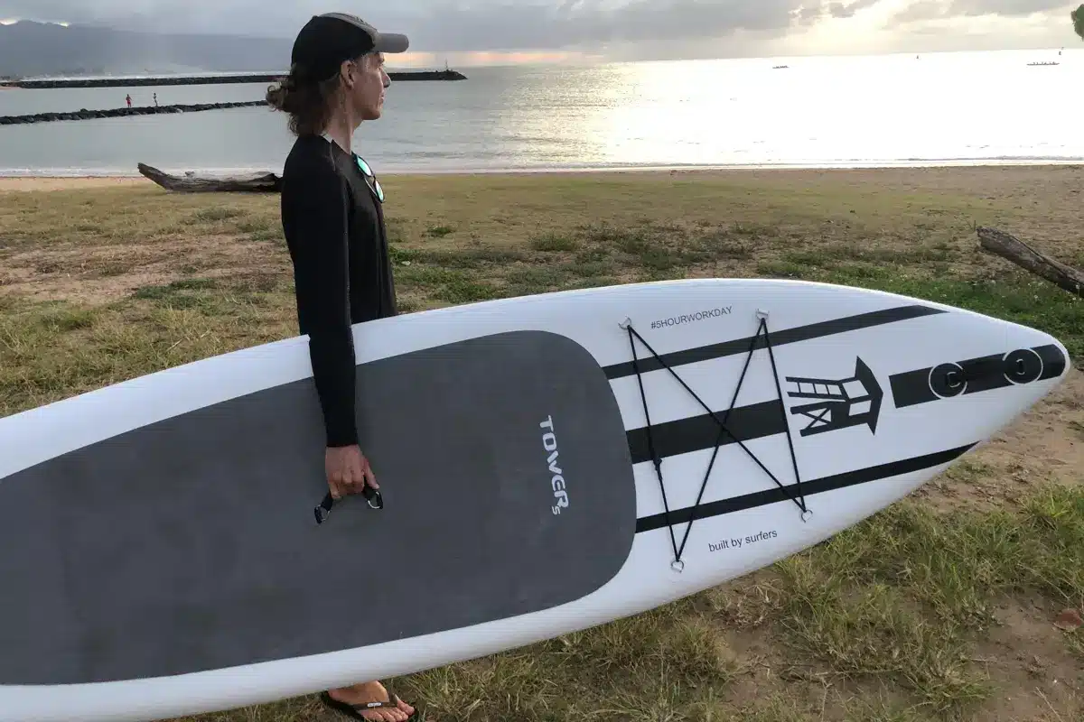 A man carrying a black and white paddle board to the beach at sunset B