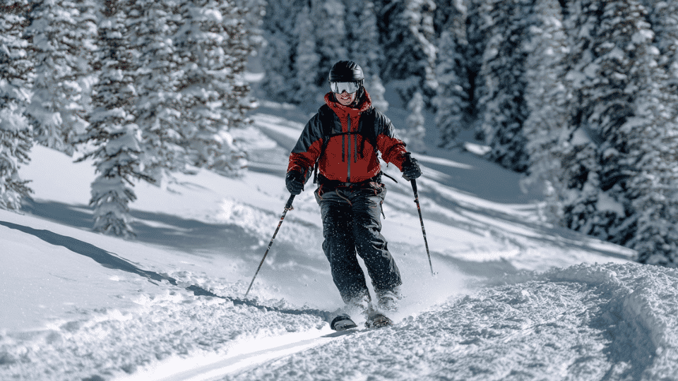Skier in proper winter skiing gear skiing across a snowy mountain trail on a bright winter day