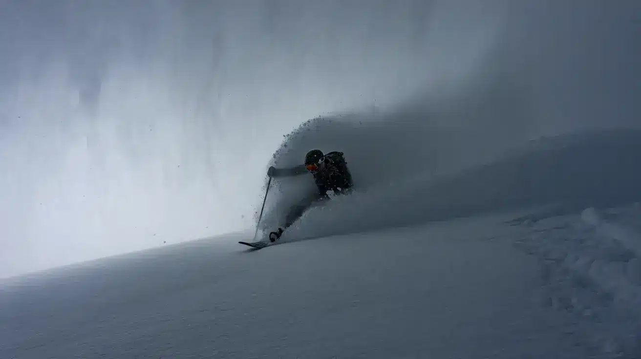 Snowboarder carving through deep powder, creating a large spray of snow on a steep slope