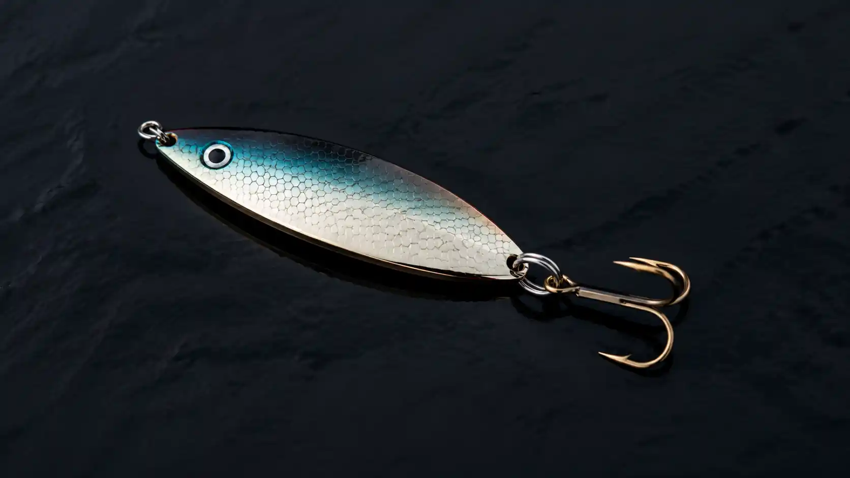 Close-up of fishing spoon lure for striped bass, metallic finish, treble hook, baitfish pattern macro detail.