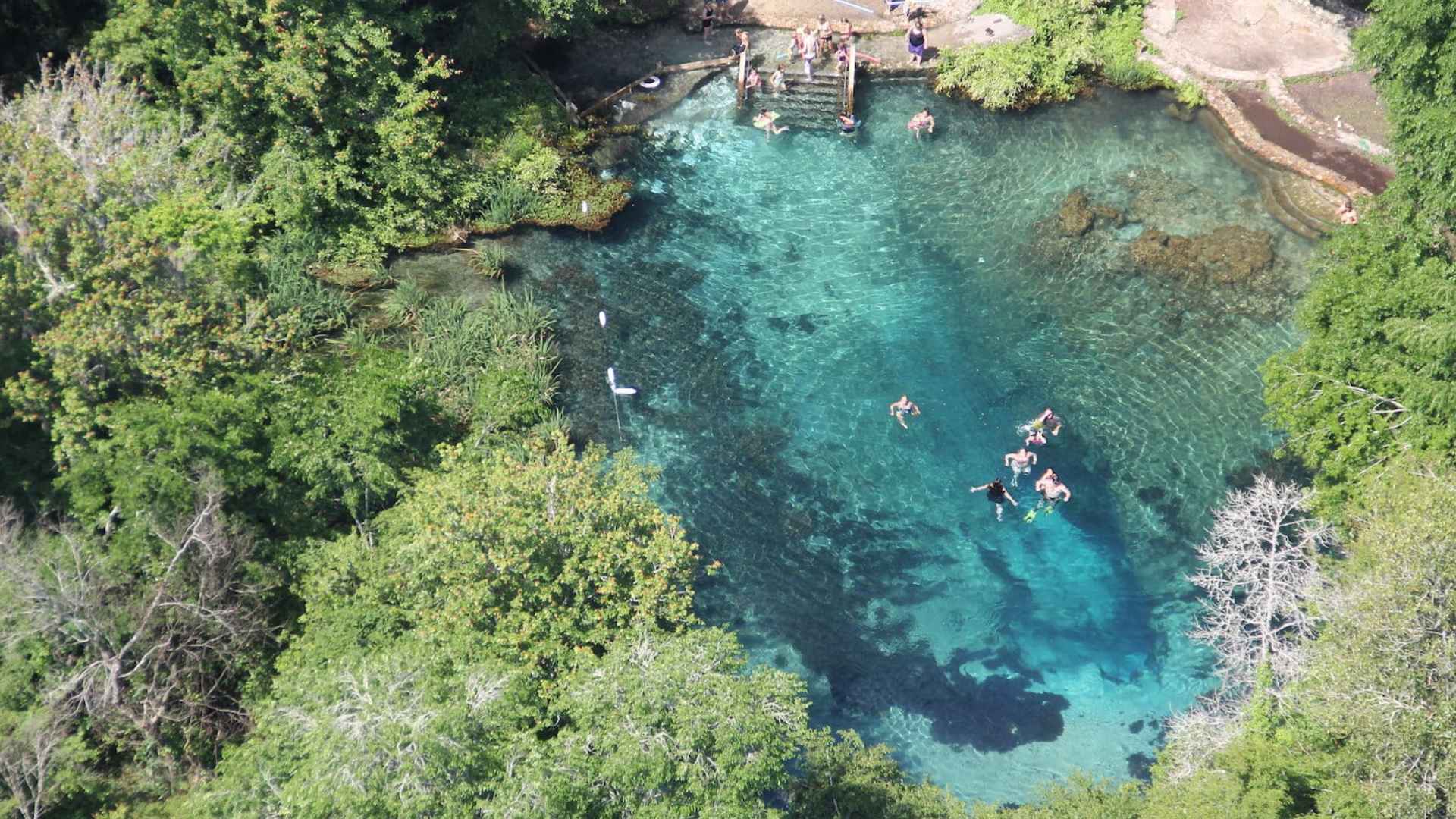 people floating in inner tubes on a clear shallow river with rocks visible and gentle current in summer day