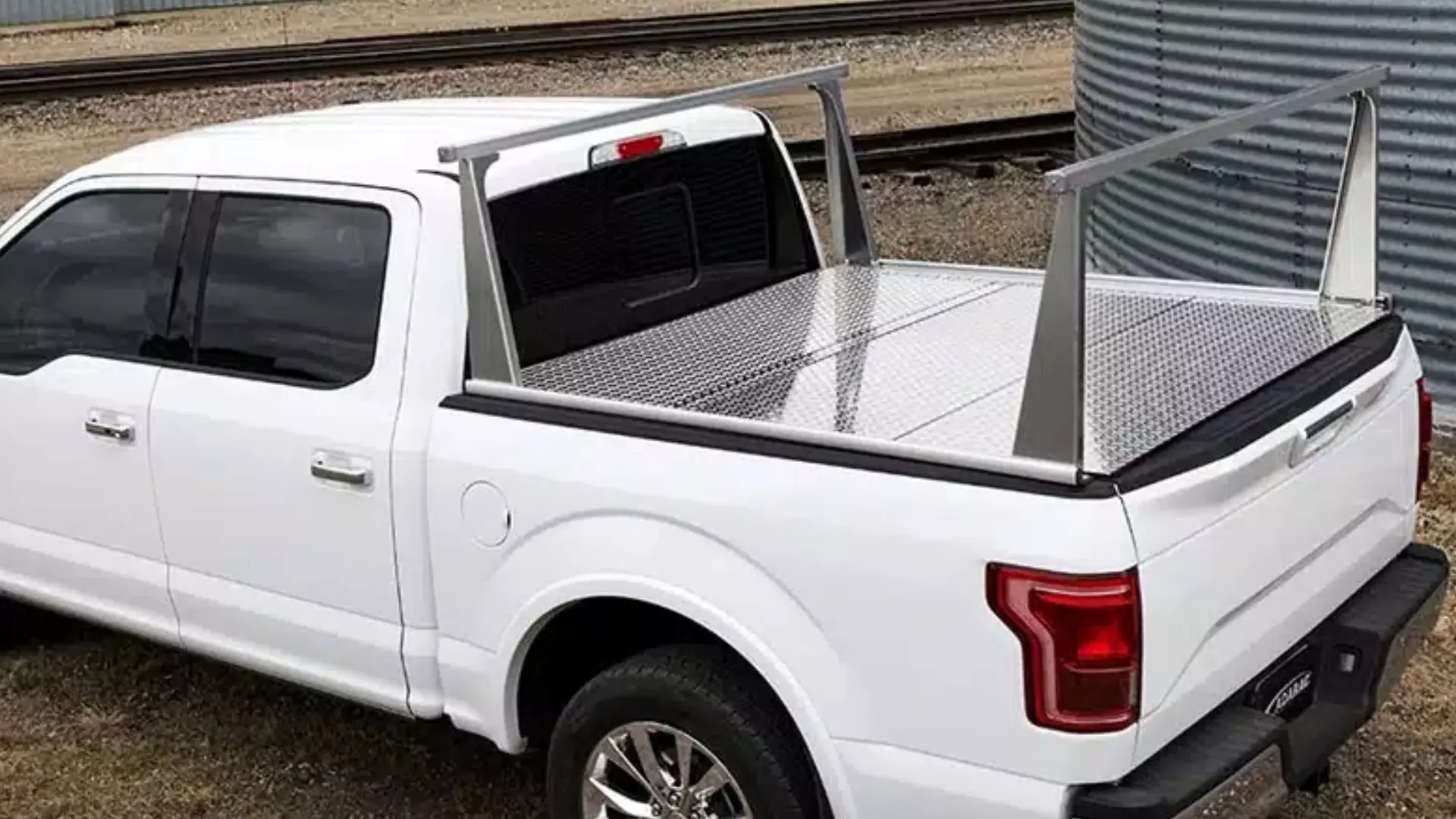 An aluminum ladder rack installed over a diamond-plate tonneau cover on a white pickup truck.