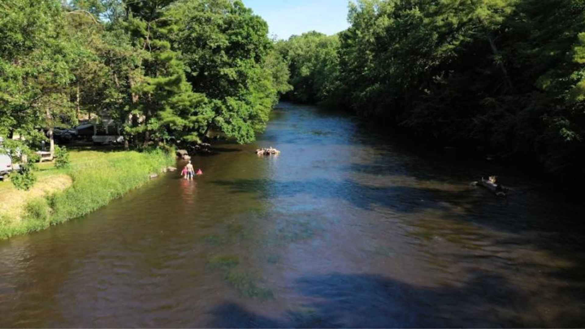 Aerial view of calm river with people floating in tubes along wooded banks on a sunny summer day