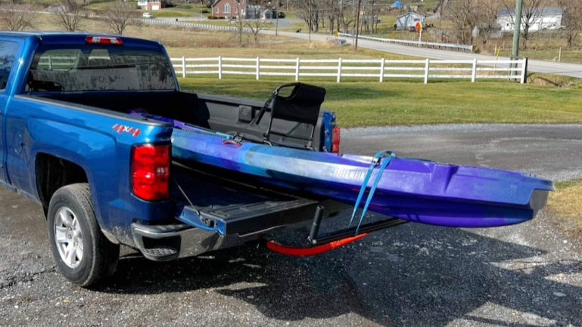 A purple kayak secured on a Boonedox Groovy T-Bone Bed Extender in the back of a blue pickup truck.