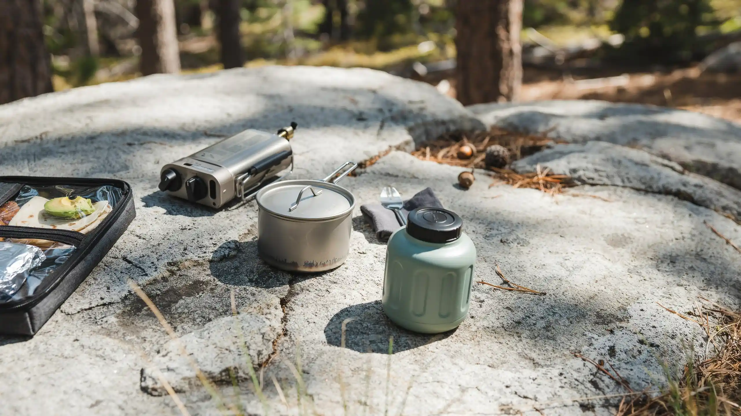 Backcountry cooking gear including stove, pot, and food storage setup on a rocky outdoor surface.