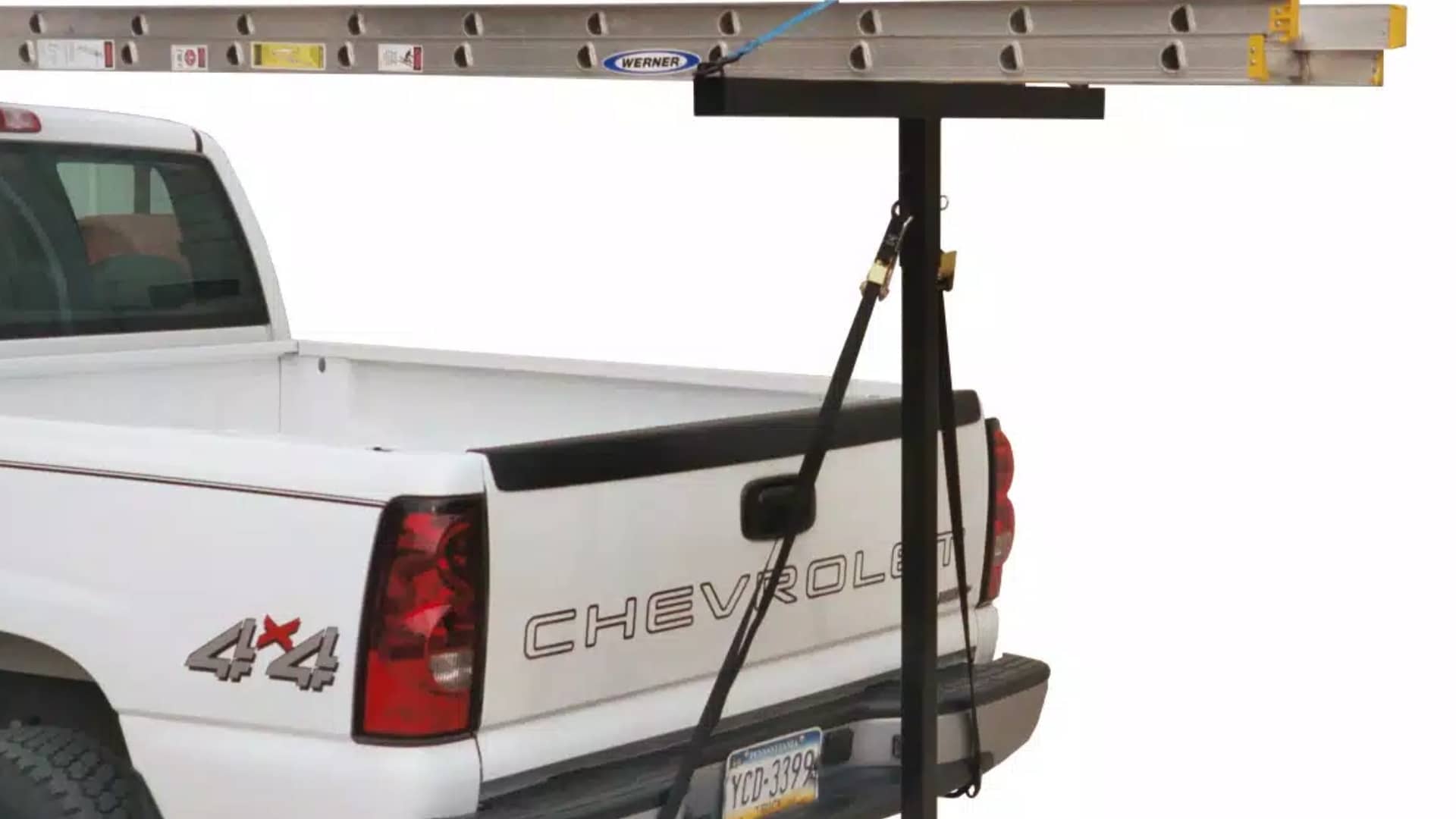 A long extension ladder supported by a Darby Extend-A-Truck hitch rack on a white pickup truck.