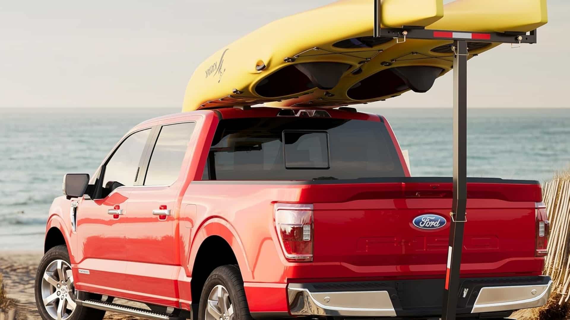 Two yellow kayaks supported by an ECOTRIC truck bed extender on a red Ford F-150 parked by the ocean.