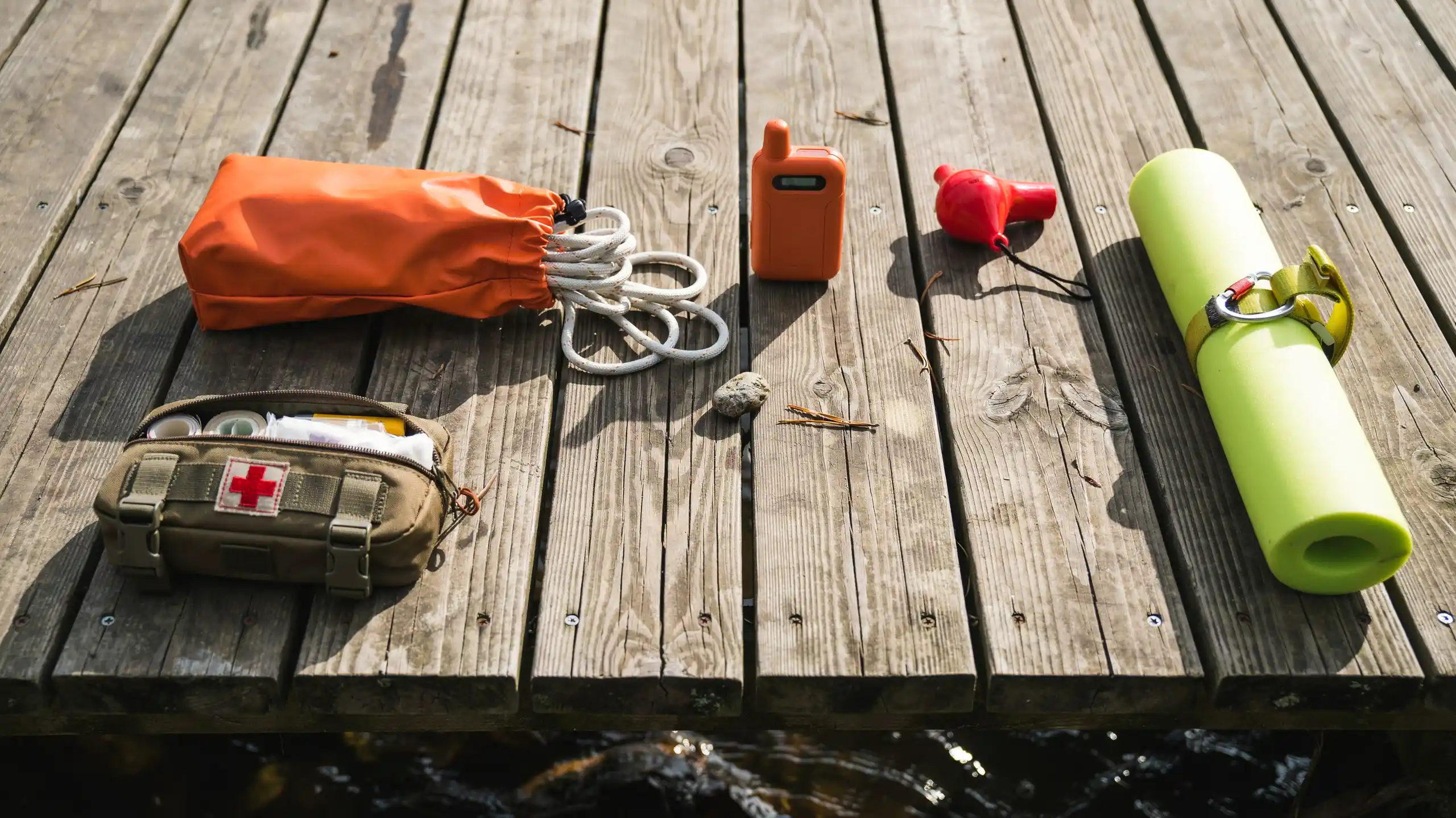 Canoeing safety gear including first aid kit, rope, whistle, and emergency equipment on wooden dock.