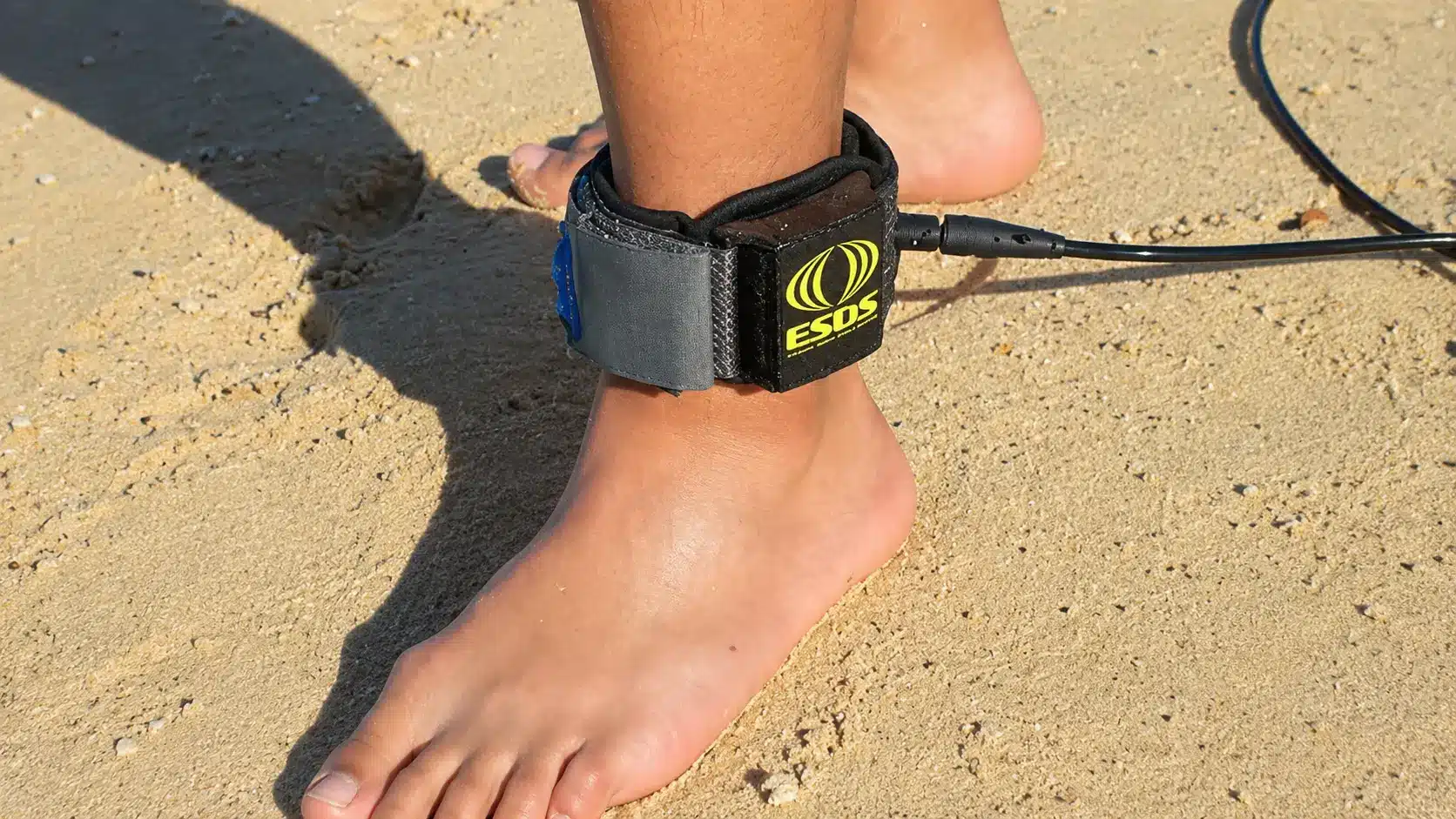 Shark protection ankle strap attached to surfer’s leg on sandy beach