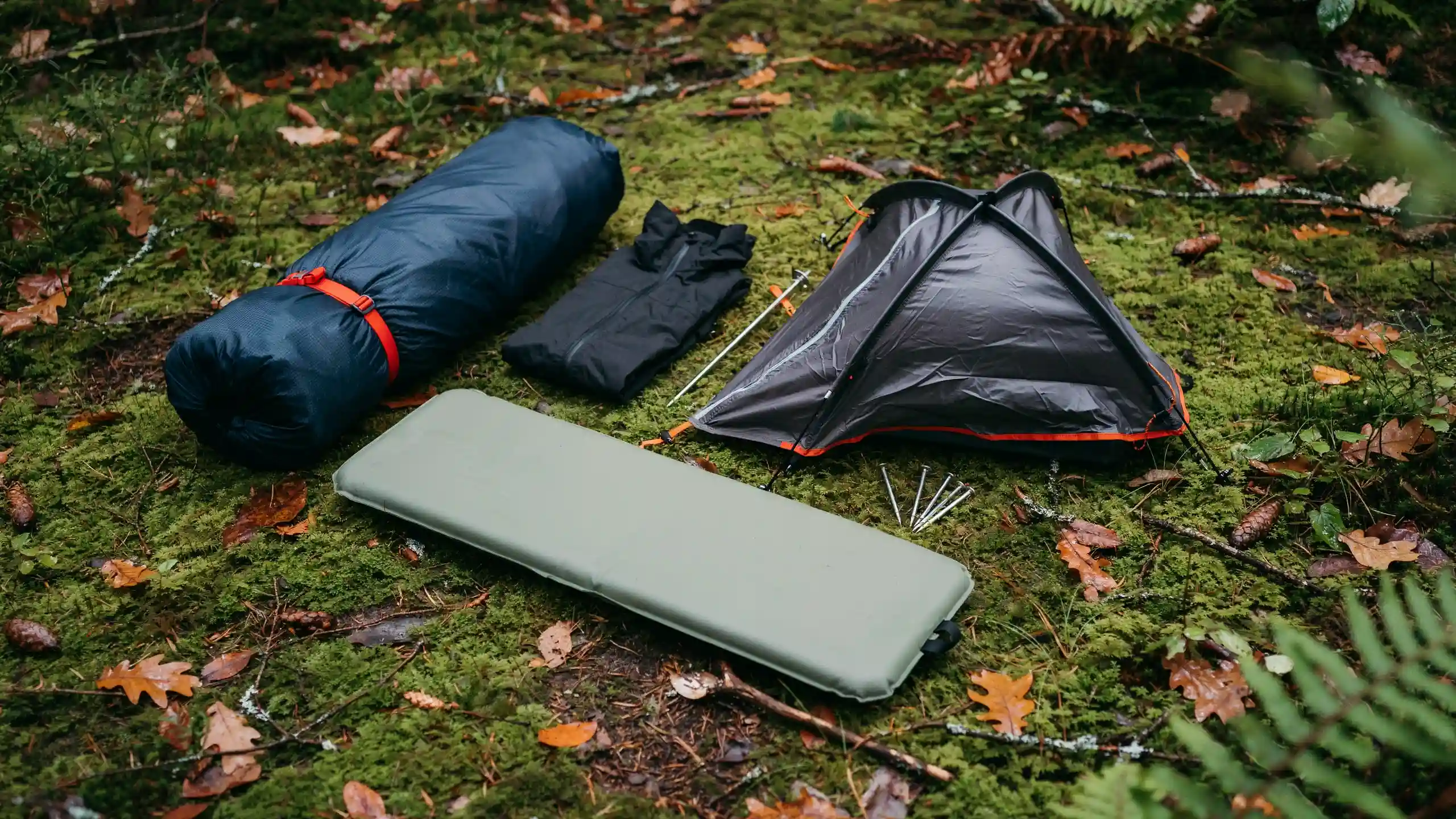 Camping tent, sleeping bag, and insulated gear arranged on forest ground for canoe camping trip.