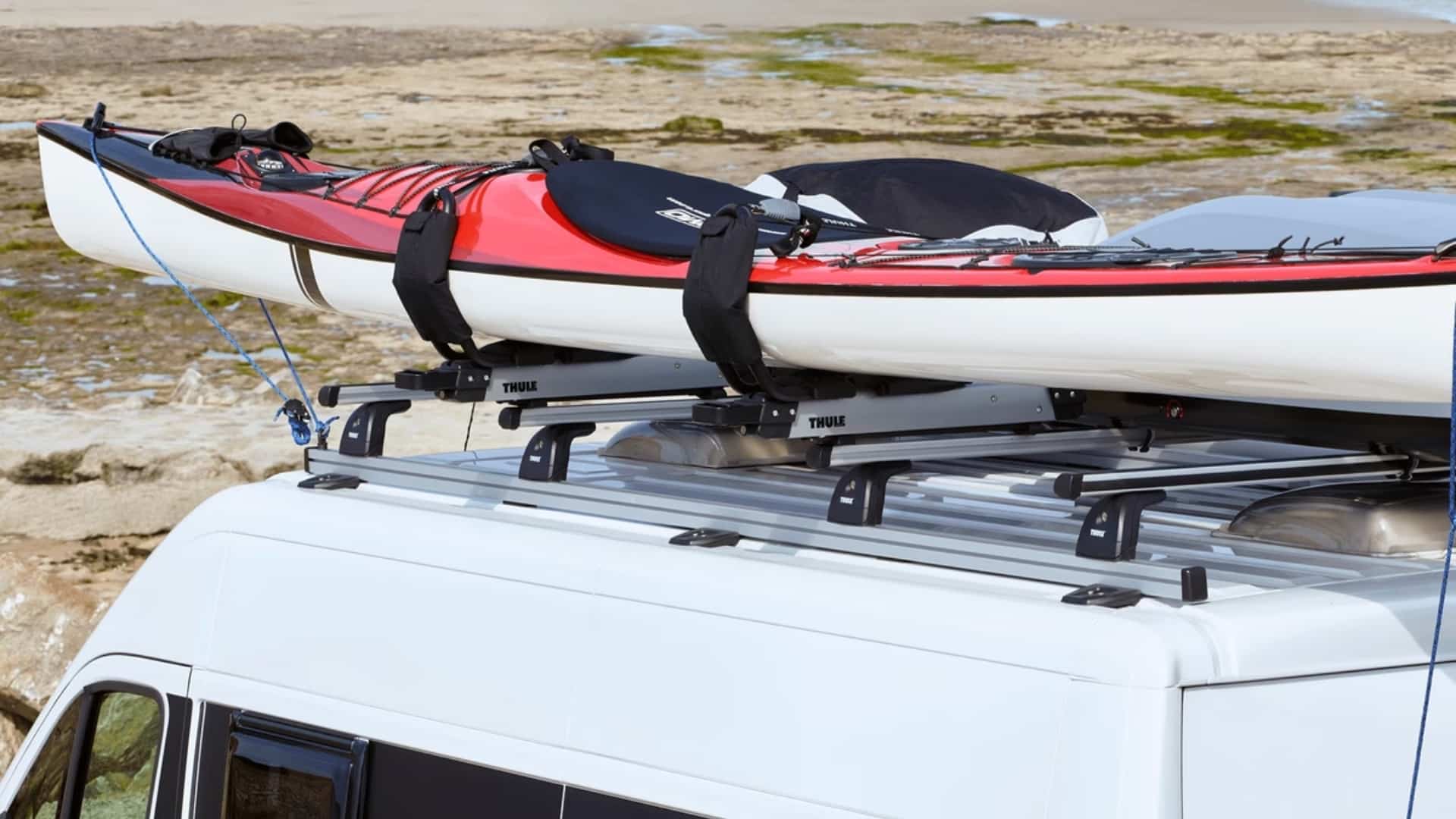 A red and white kayak secured to a Thule roof rack system on top of a white van.