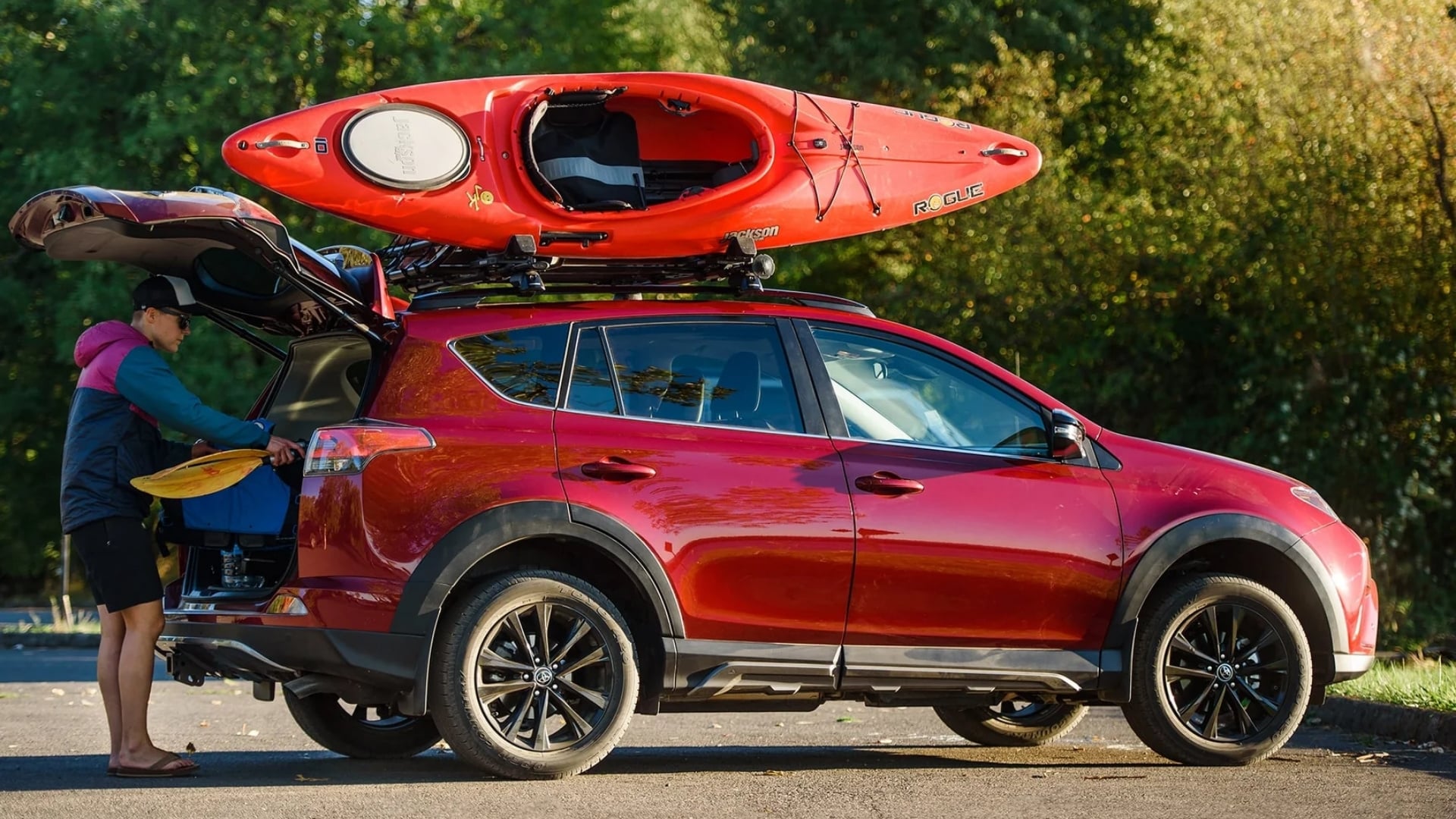 A red kayak mounted on a Yakima JayLow roof rack atop a red SUV with its trunk open.
