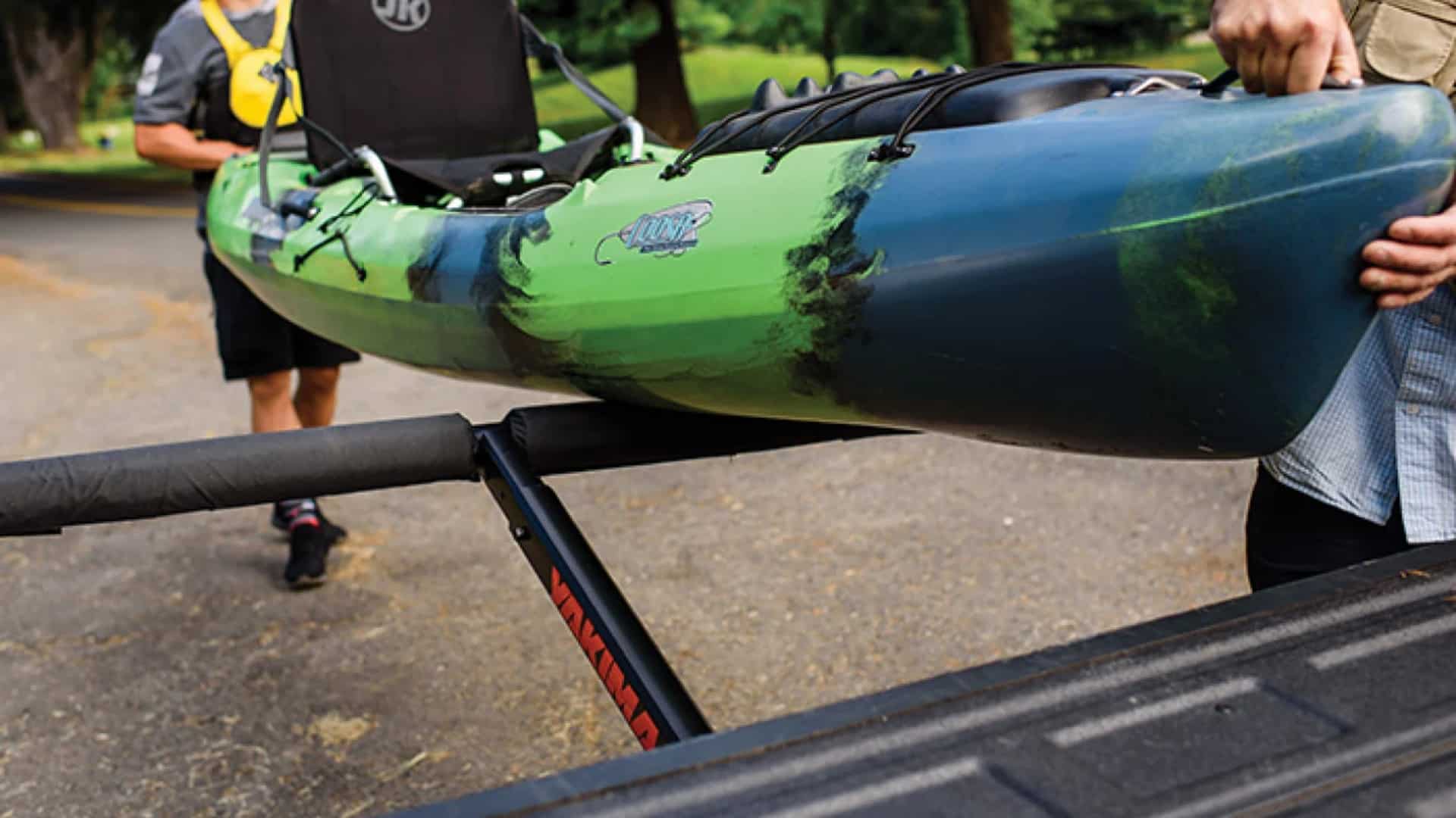 Two people loading a green and blue kayak onto a Yakima truck bed extender.