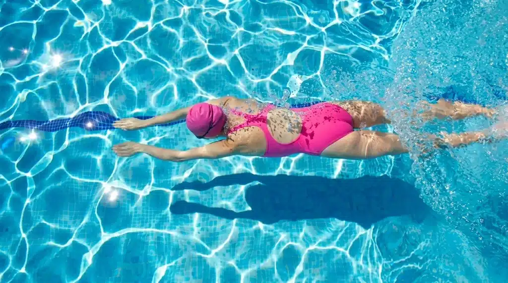 Swimmer in pink cap and swimsuit moving through a clear blue pool during a lap swim.