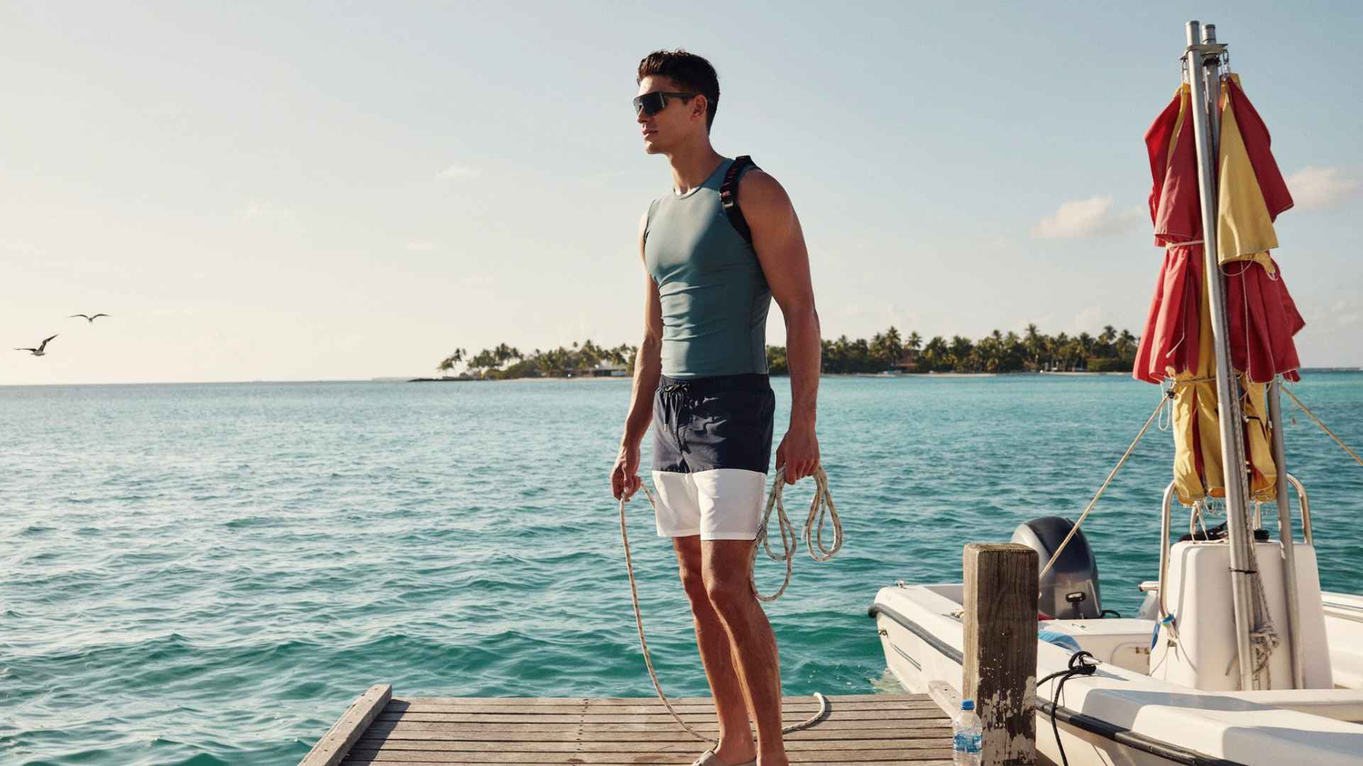 Man wearing board shorts and swimwear with accessories ready for a parasailing adventure