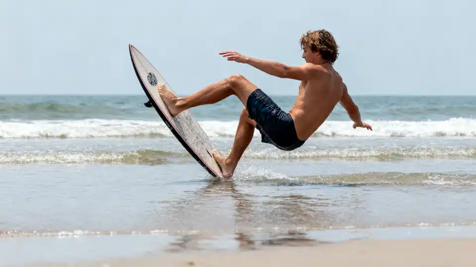 Skimboarder performing a 180 spin on shallow water with the board turning and body balanced naturally