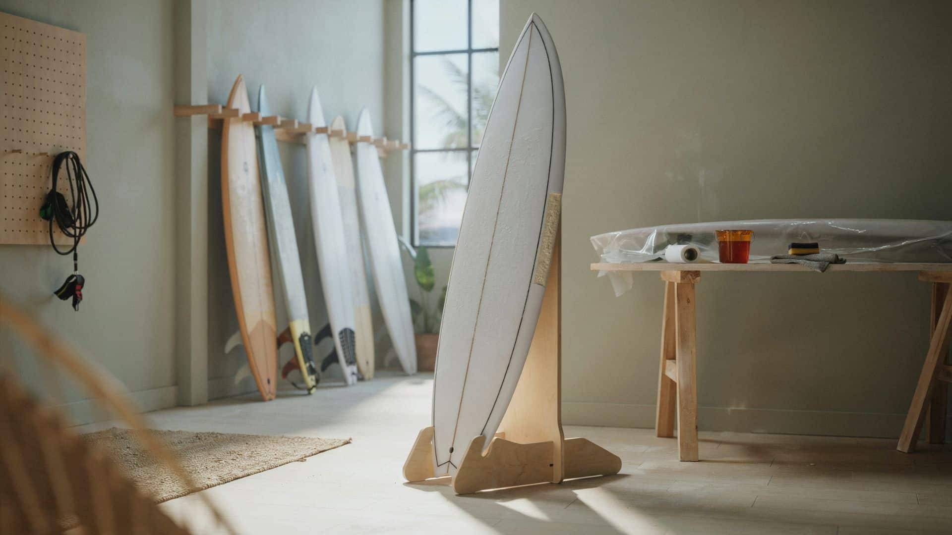 White EPS epoxy surfboard displayed upright on a wooden stand in a workshop