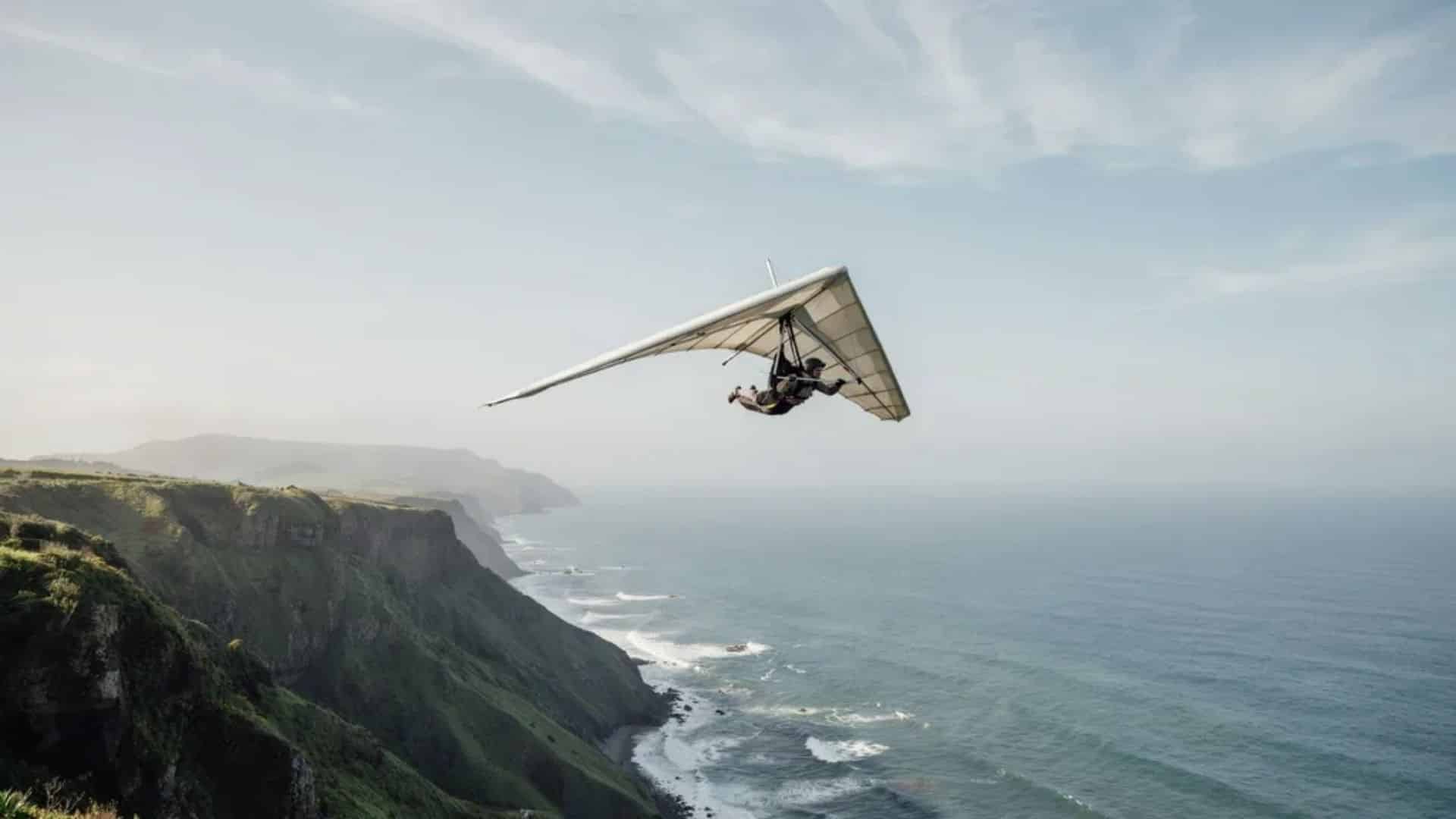 Hang glider pilot in realistic forward flight over coastal cliffs above ocean