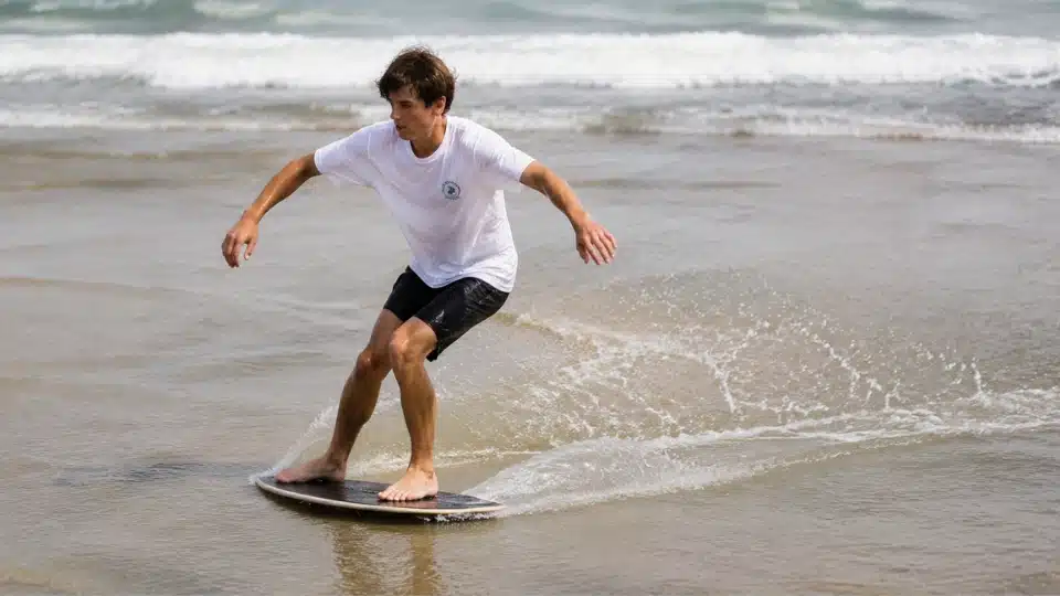 Beginner skimboarder standing on a moving board with balanced posture while gliding across shallow water