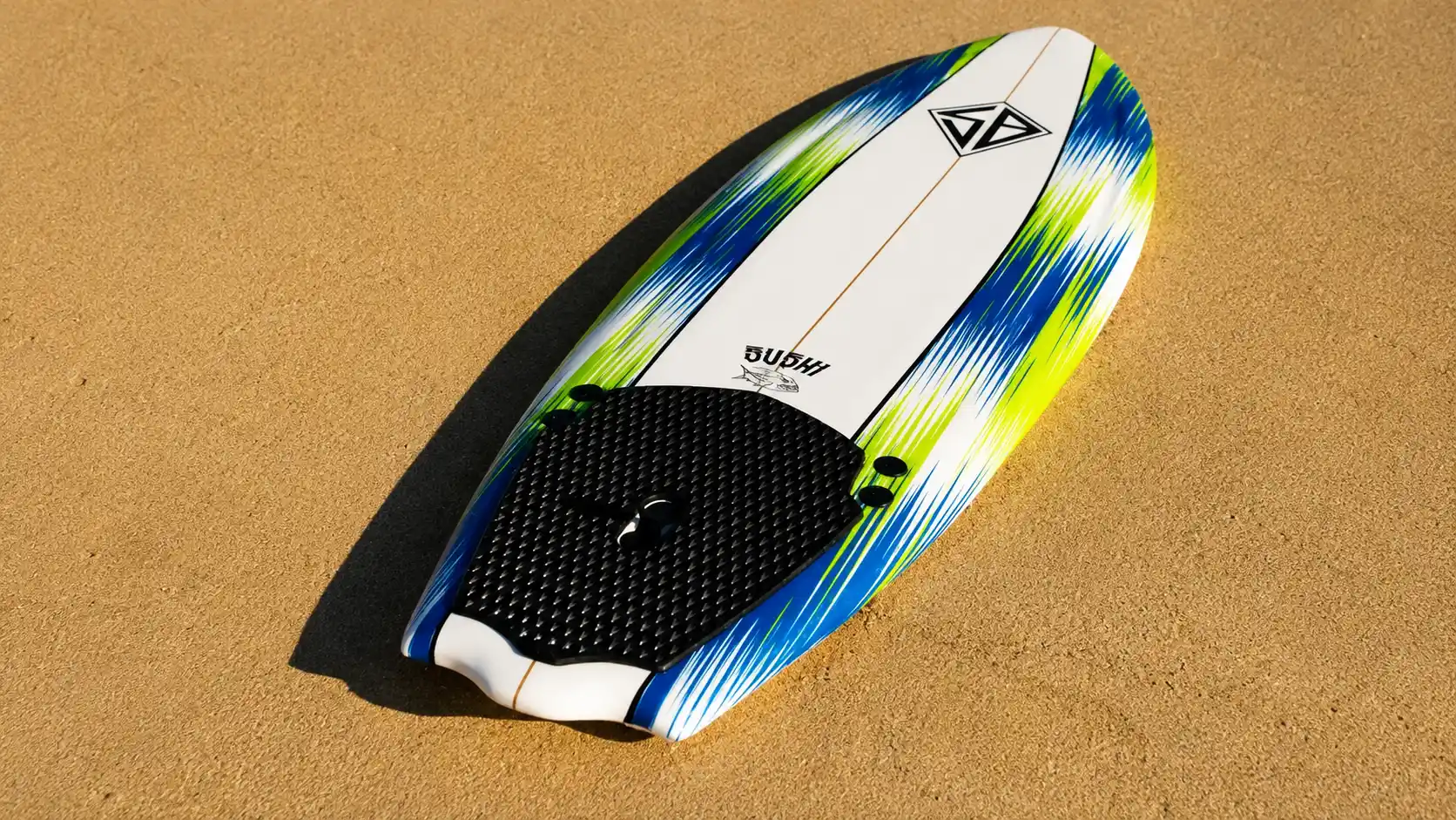 Colorful Costco surfboard with black traction pad resting diagonally on the warm sand under bright beach sunlight