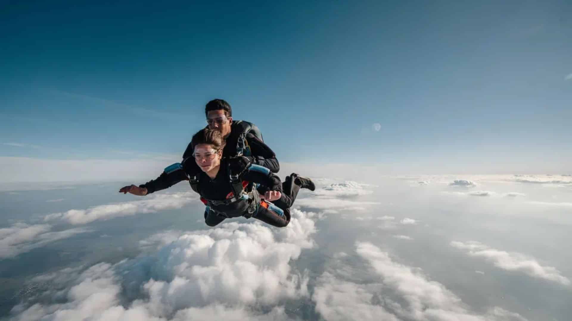 Tandem skydivers in free fall above clouds before parachute deployment